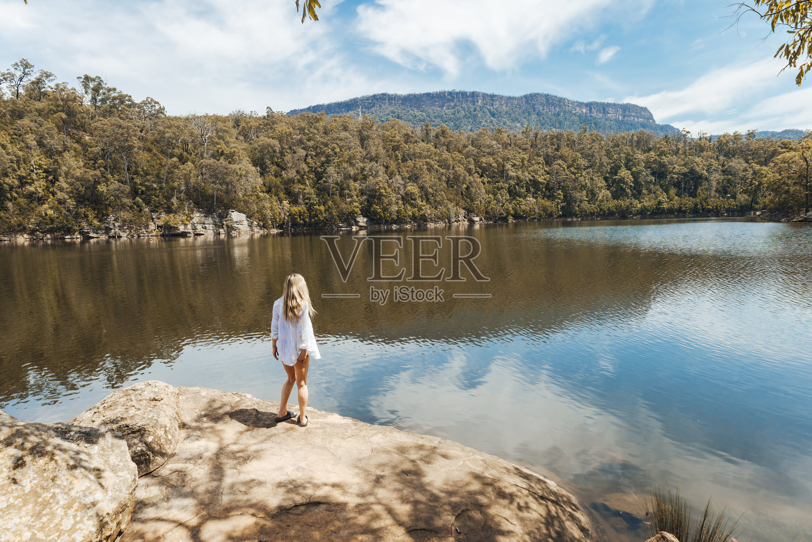 身穿飘逸白衬衫的女子站在河边的岩石上照片摄影图片