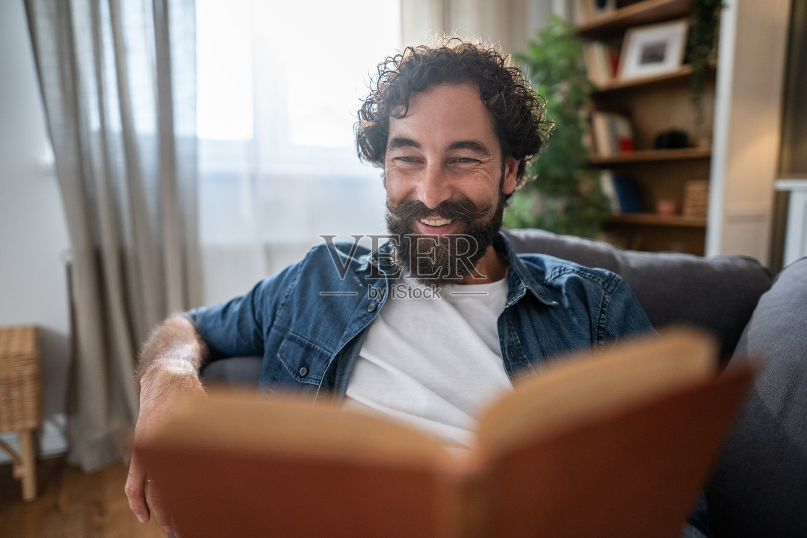 快乐的男人在家里的沙发上放松地看书照片摄影图片