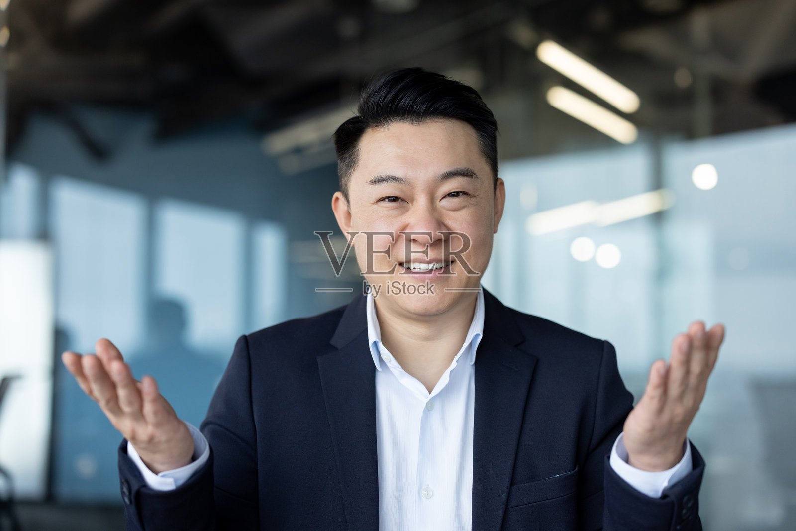 一位年轻的亚洲商人坐在办公室里，面朝镜头，用手比划着交谈的特写肖像照片摄影图片