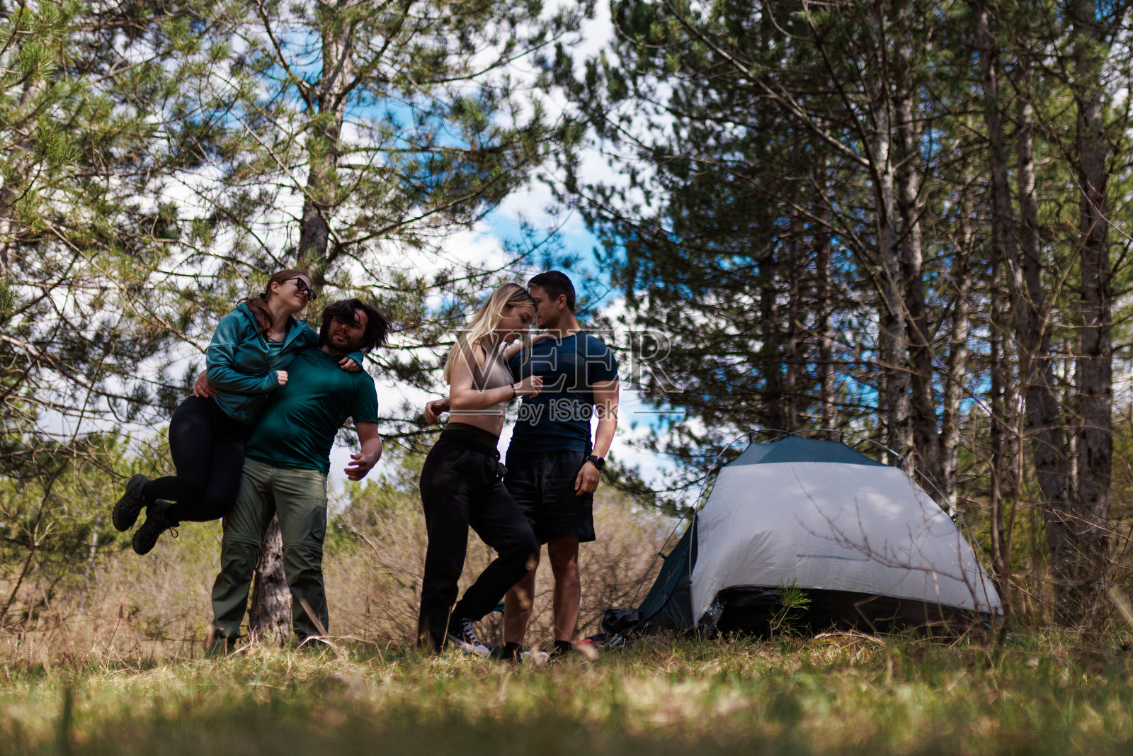 朋友们在阳光明媚的日子里，于高大树木和自然环绕的林地中，享受着热闹的露营之旅。照片摄影图片