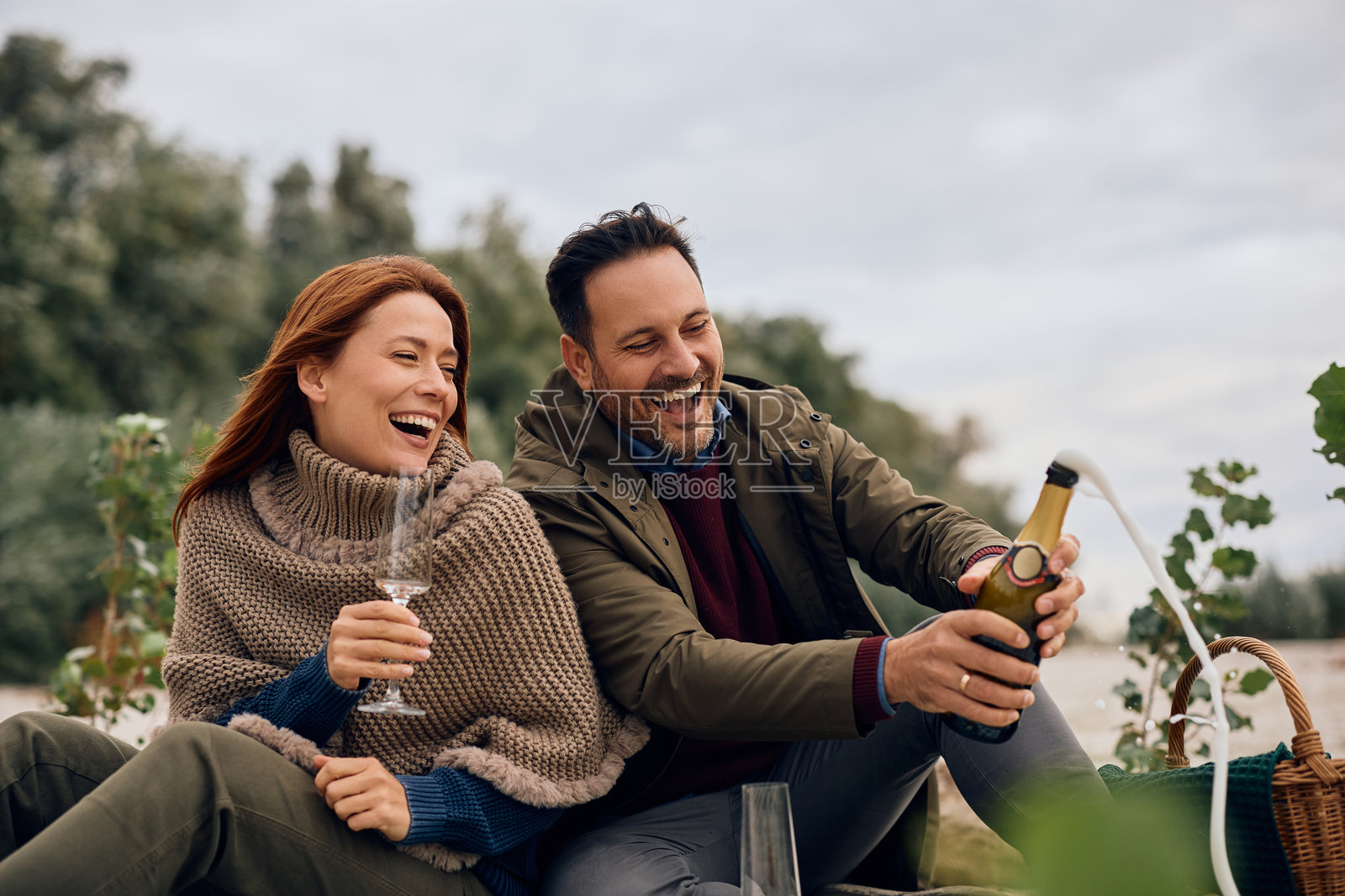 秋日野餐时，一对快乐的夫妇正在打开香槟。照片摄影图片