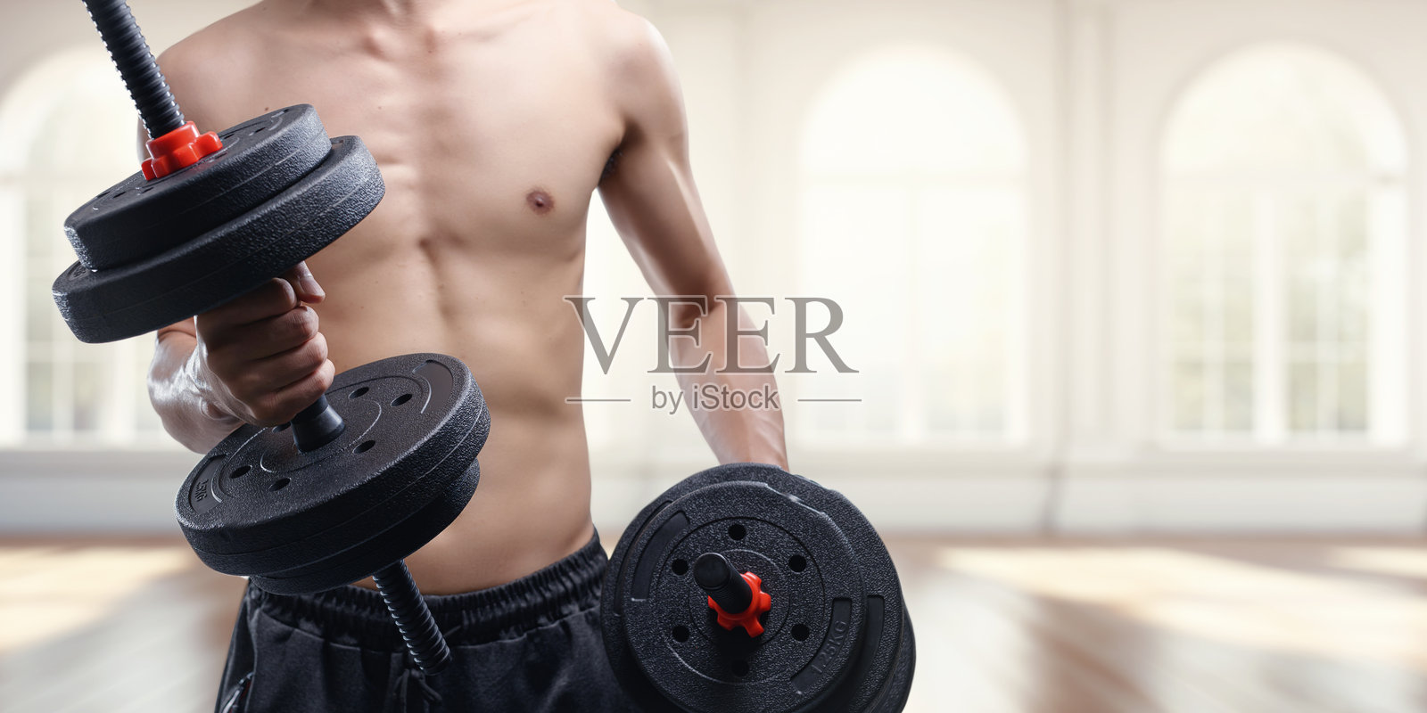 明亮室内空间里，身材健美的个人正在举重哑铃照片摄影图片