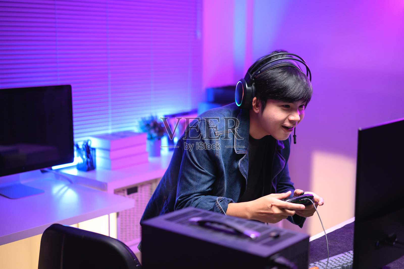 一个年轻男子在霓虹灯照耀的房间里享受玩电脑游戏。游戏氛围充满活力色彩。照片摄影图片