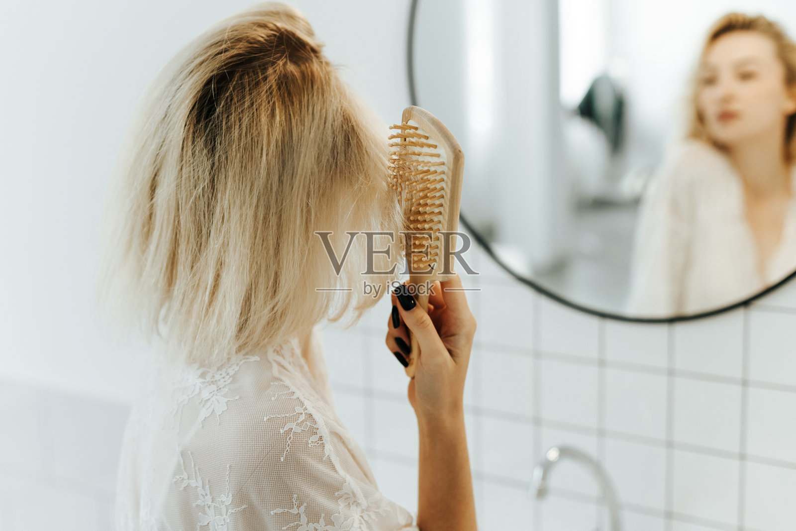 身穿白色内衣的美丽年轻女子，在浴室对着镜子梳头并微笑，这是她的背影。照片摄影图片