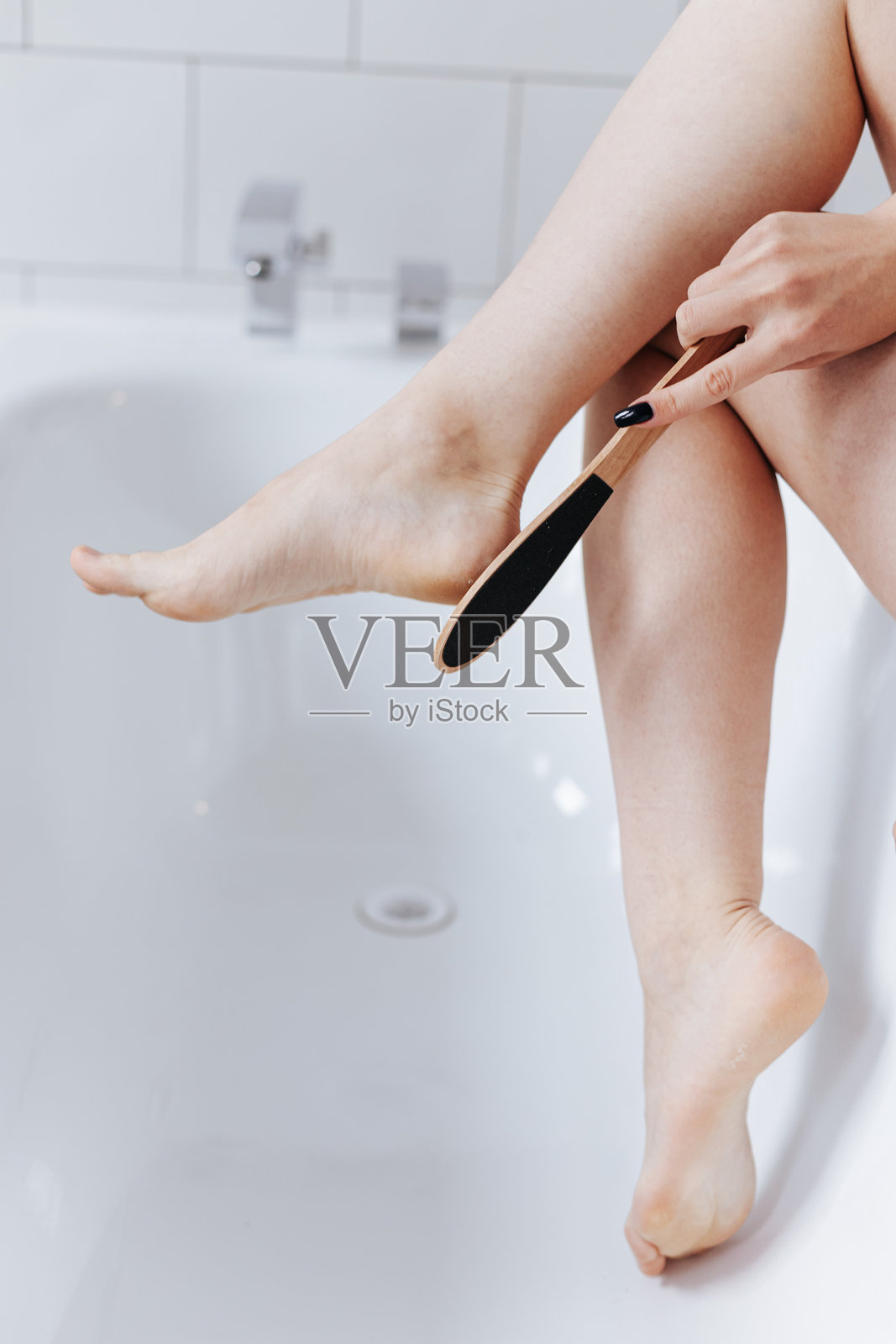 年轻女子在浴室用足跟刷清洁她的脚照片摄影图片