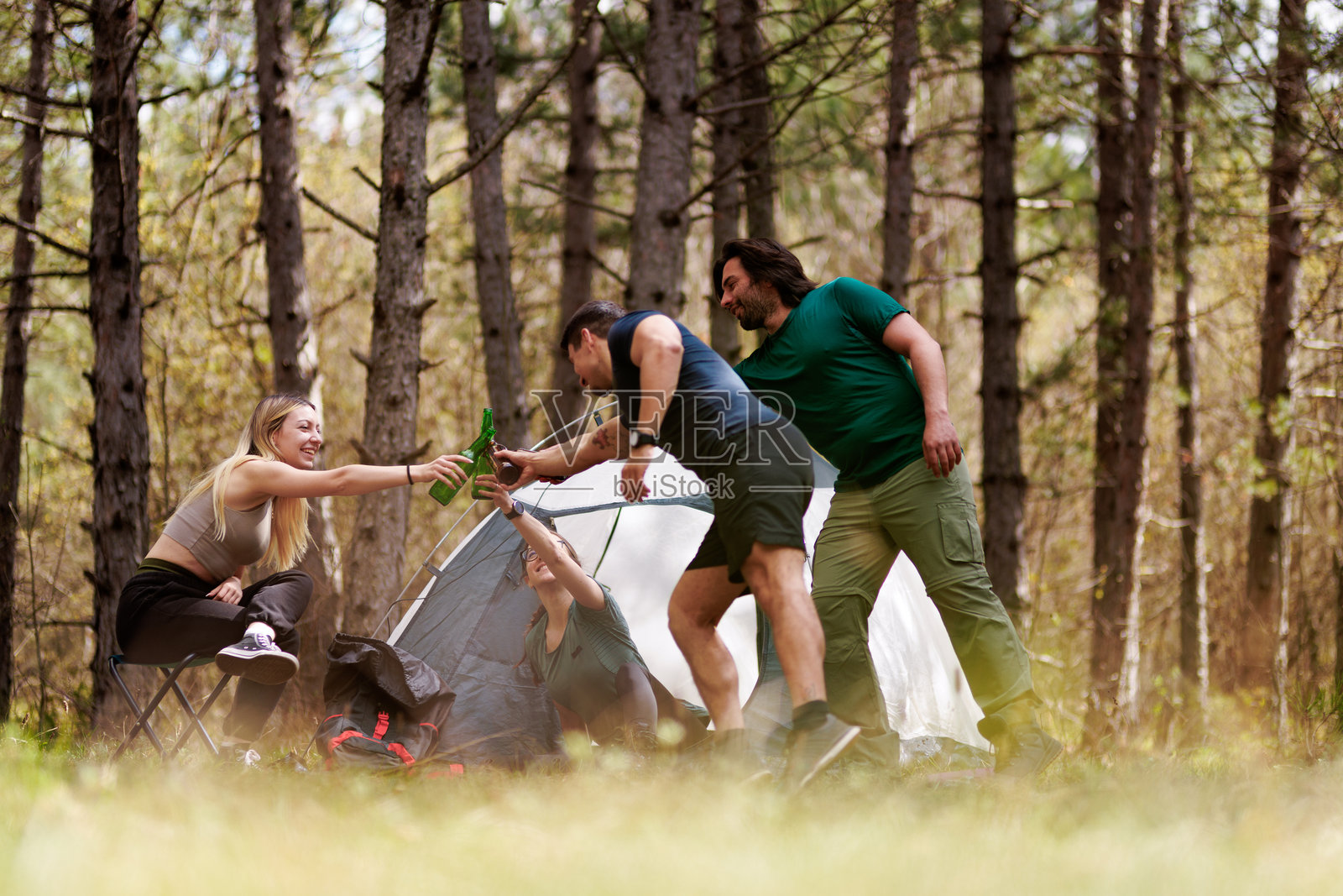 在阳光明媚的下午，朋友们在宁静的森林里露营，周围是高大的树木，他们一边畅饮一边欢笑照片摄影图片