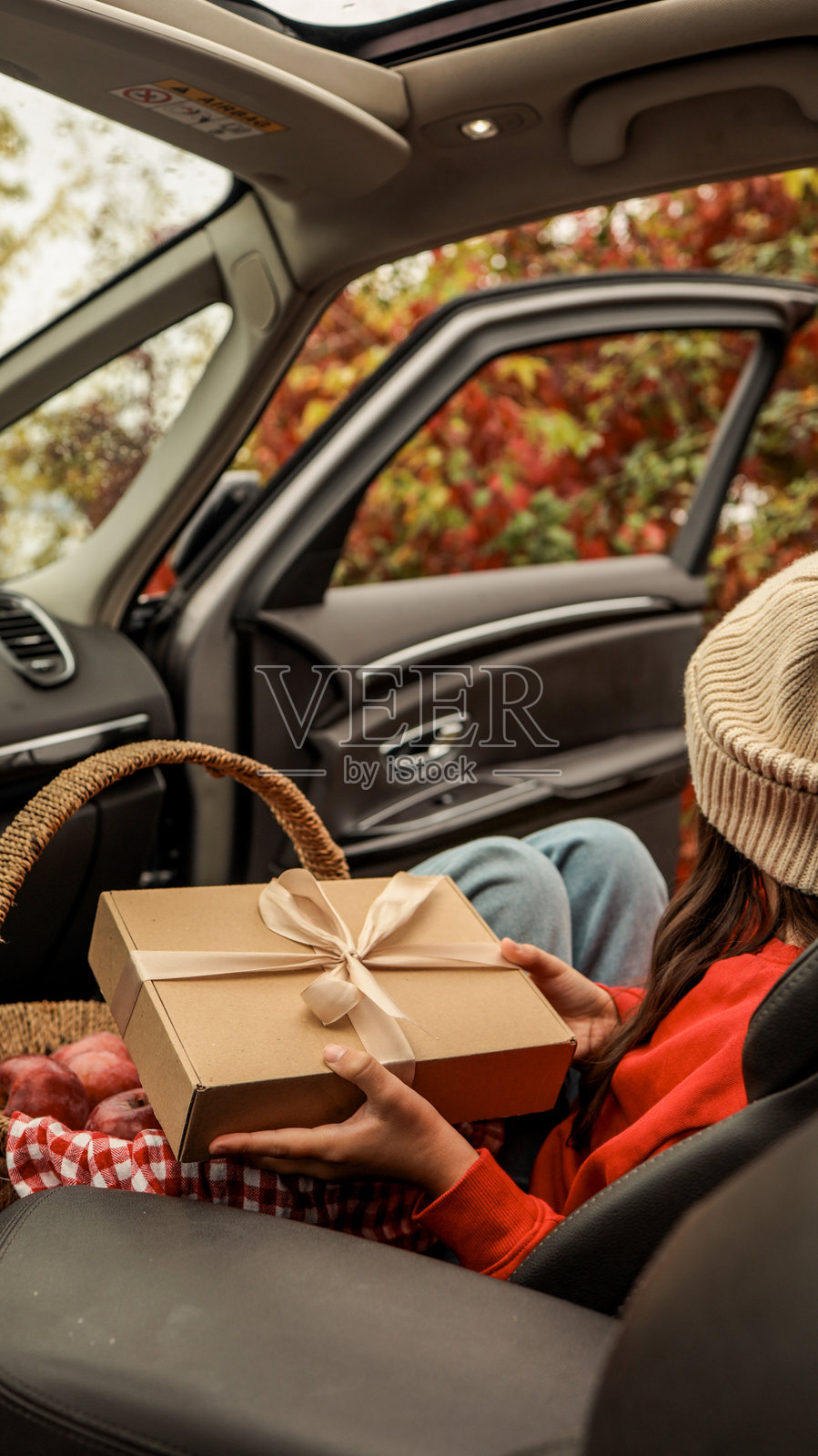 一个人坐在车里，手里拿着一个礼物盒，旁边还有一篮苹果。照片摄影图片