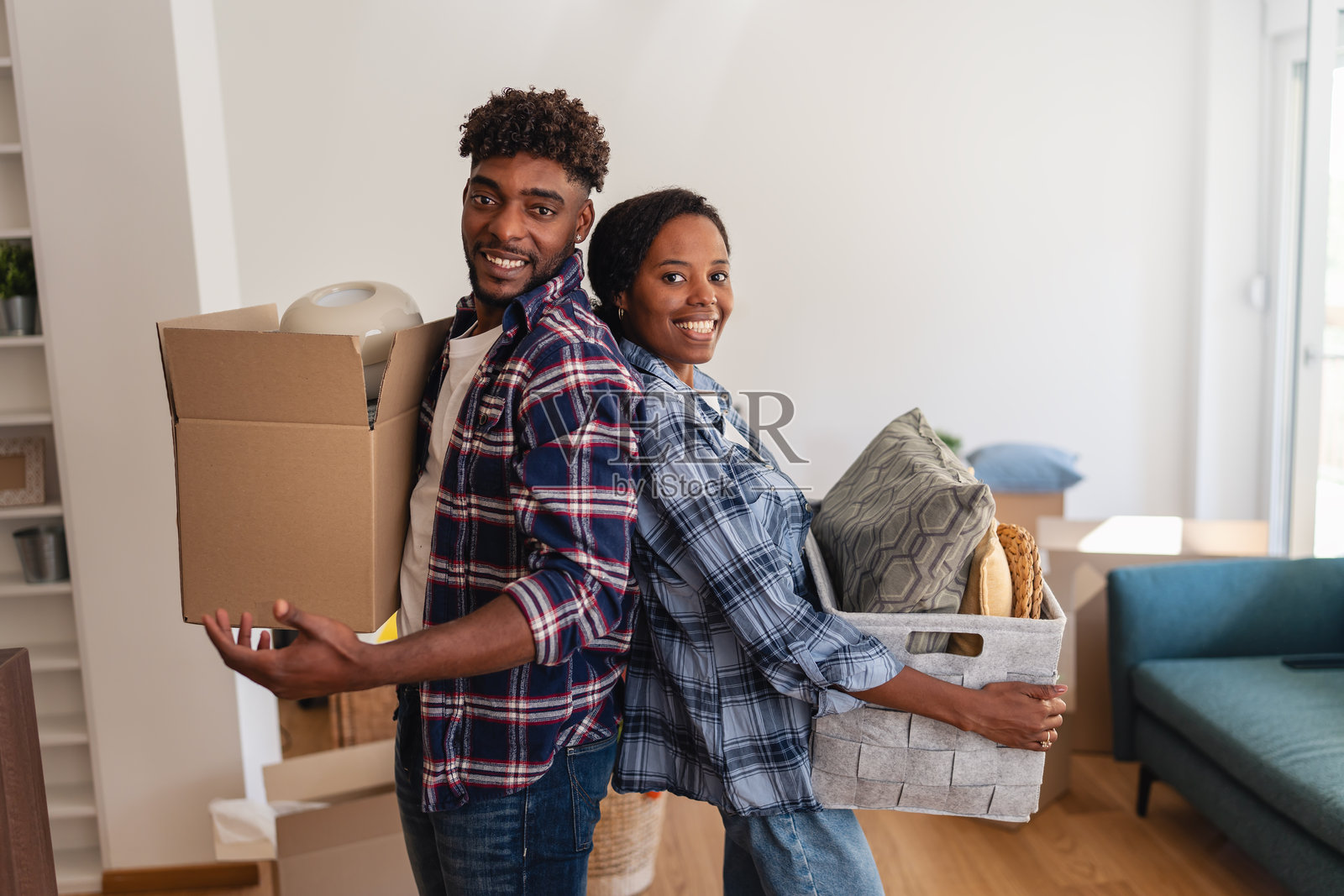 一对非洲裔美国情侣在他们的新公寓里背靠背站着，手里拿着箱子和家居装饰品，在搬家后进行拆包和整理。照片摄影图片