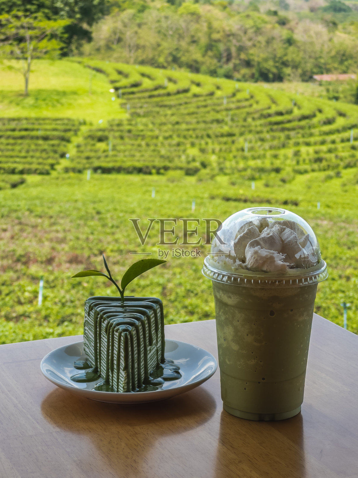 享用美味的抹茶千层蛋糕，上面点缀着新鲜的茶叶，旁边还有一杯清爽的抹茶星冰乐。这道令人愉悦的甜点与饮品搭配，摆放在木桌上，俯瞰着葱郁的照片摄影图片