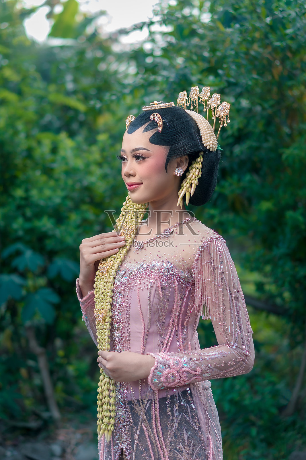 身着粉色传统爪哇卡巴雅的亚洲新娘，佩戴茉莉花发饰，妆容优雅，在户外从容地摆出姿势，表情自然，充满文化自豪感。照片摄影图片