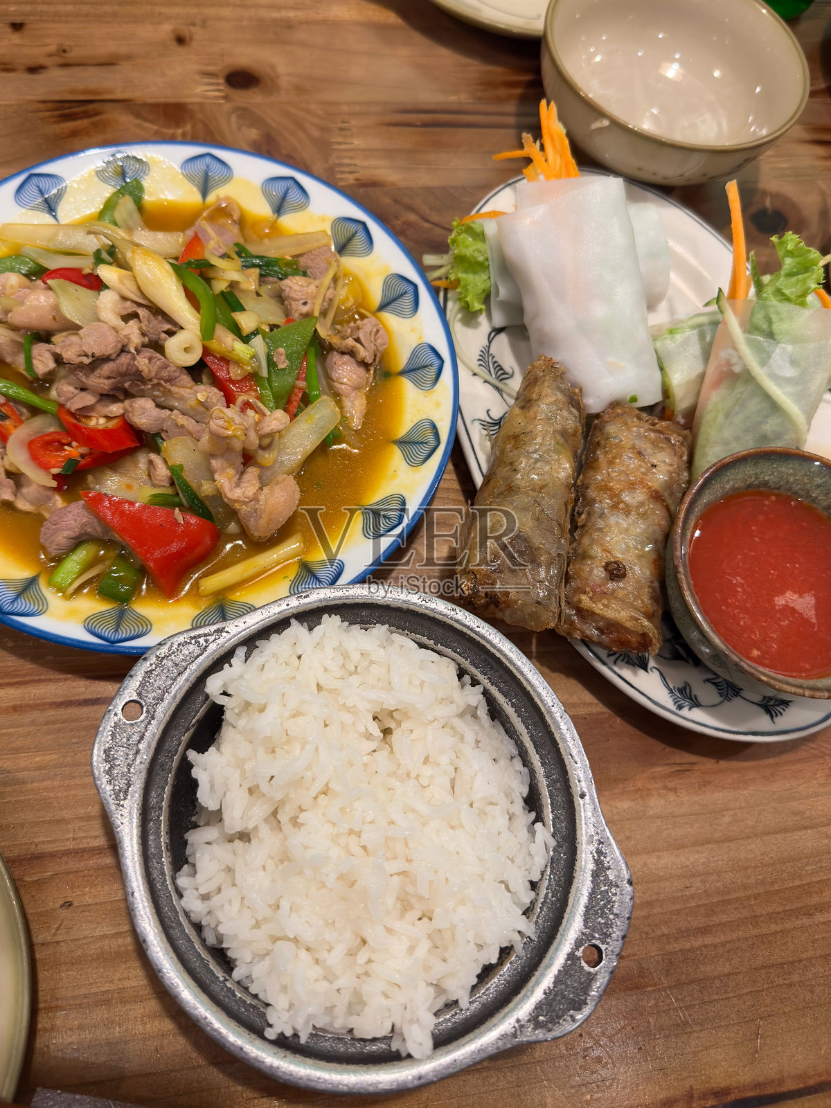 一张乡村木桌上摆放着丰盛的正宗越南美食，包括美味的炒猪肉、新鲜的春卷、香脆的炸春卷和香喷喷的米饭。照片摄影图片