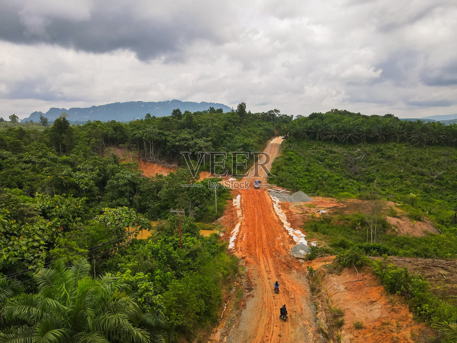 印度尼西亚婆罗洲东库泰偏远内陆地区正在修建的泥泞道路的鸟瞰图。道路穿过雨林和棕榈油种植园，地平线上是喀斯特山脉。照片摄影图片