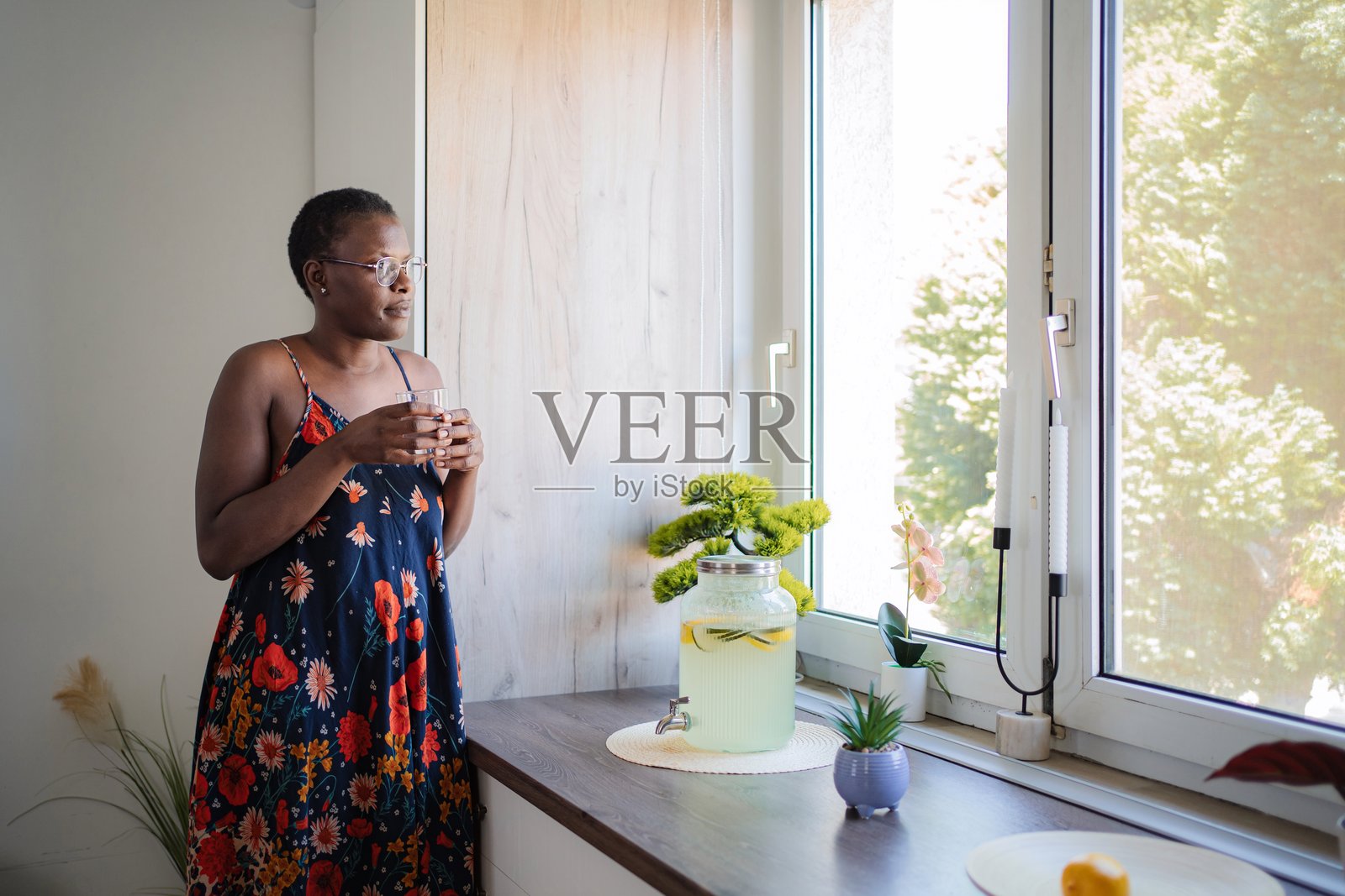 年轻女子在厨房里喝着自制柠檬水，望着窗外照片摄影图片