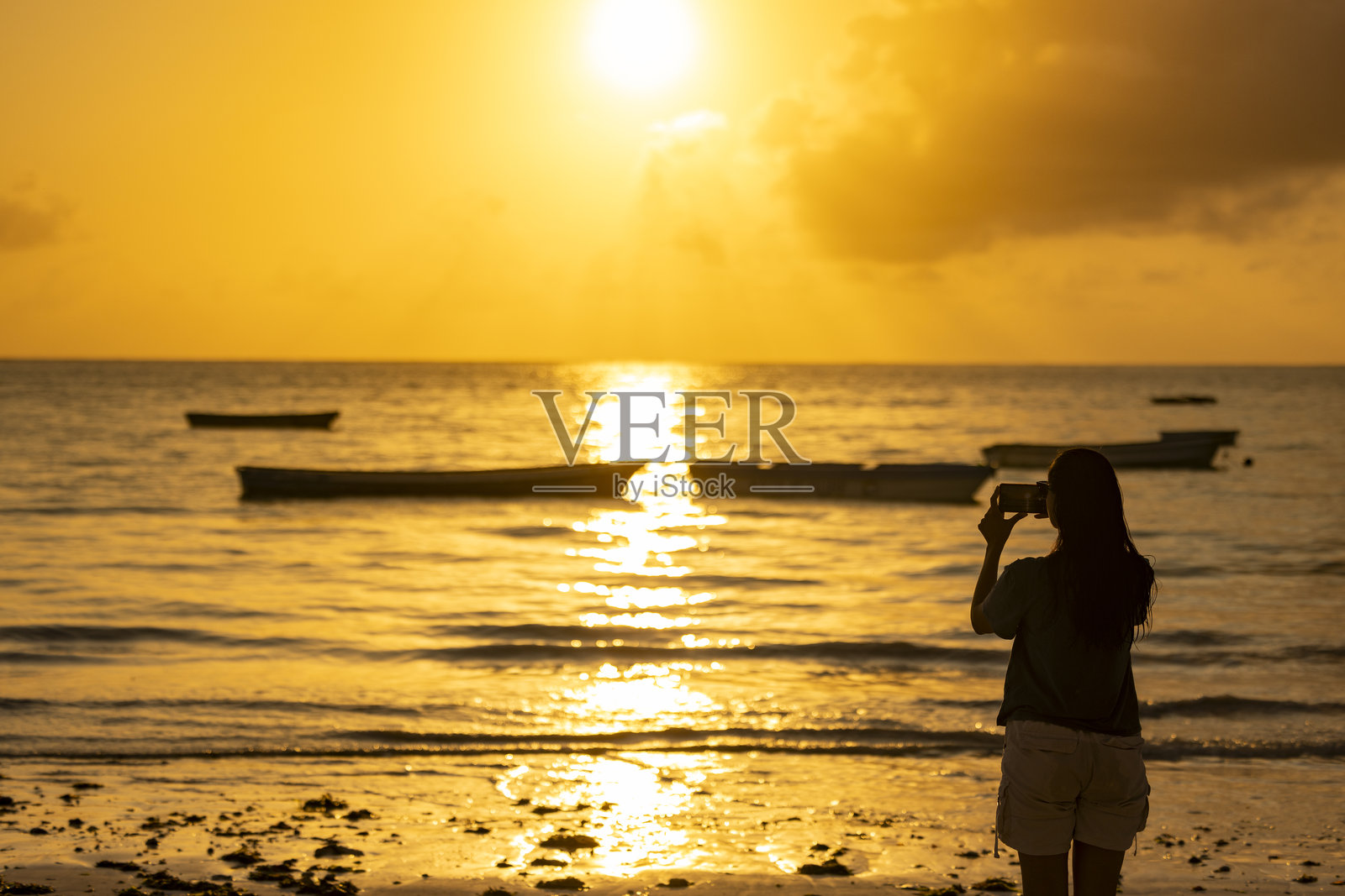 日落时分，一位女士正在拍摄海滩的景象照片摄影图片