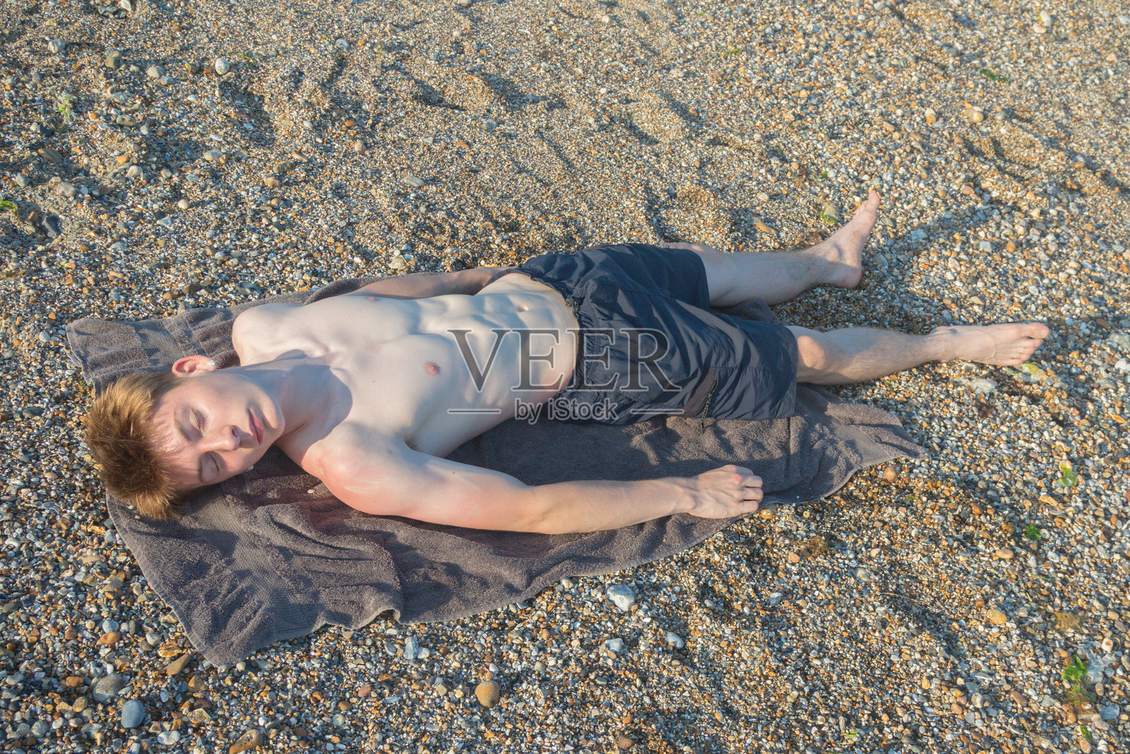 一个十几岁的男孩在海滩上晒日光浴照片摄影图片