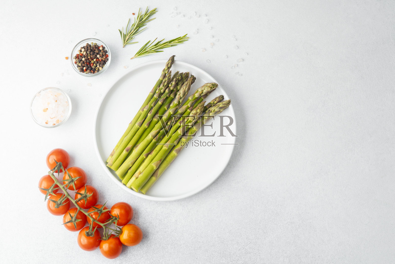 新鲜的绿色芦笋放在白盘子里，配有番茄、盐、胡椒和迷迭香照片摄影图片