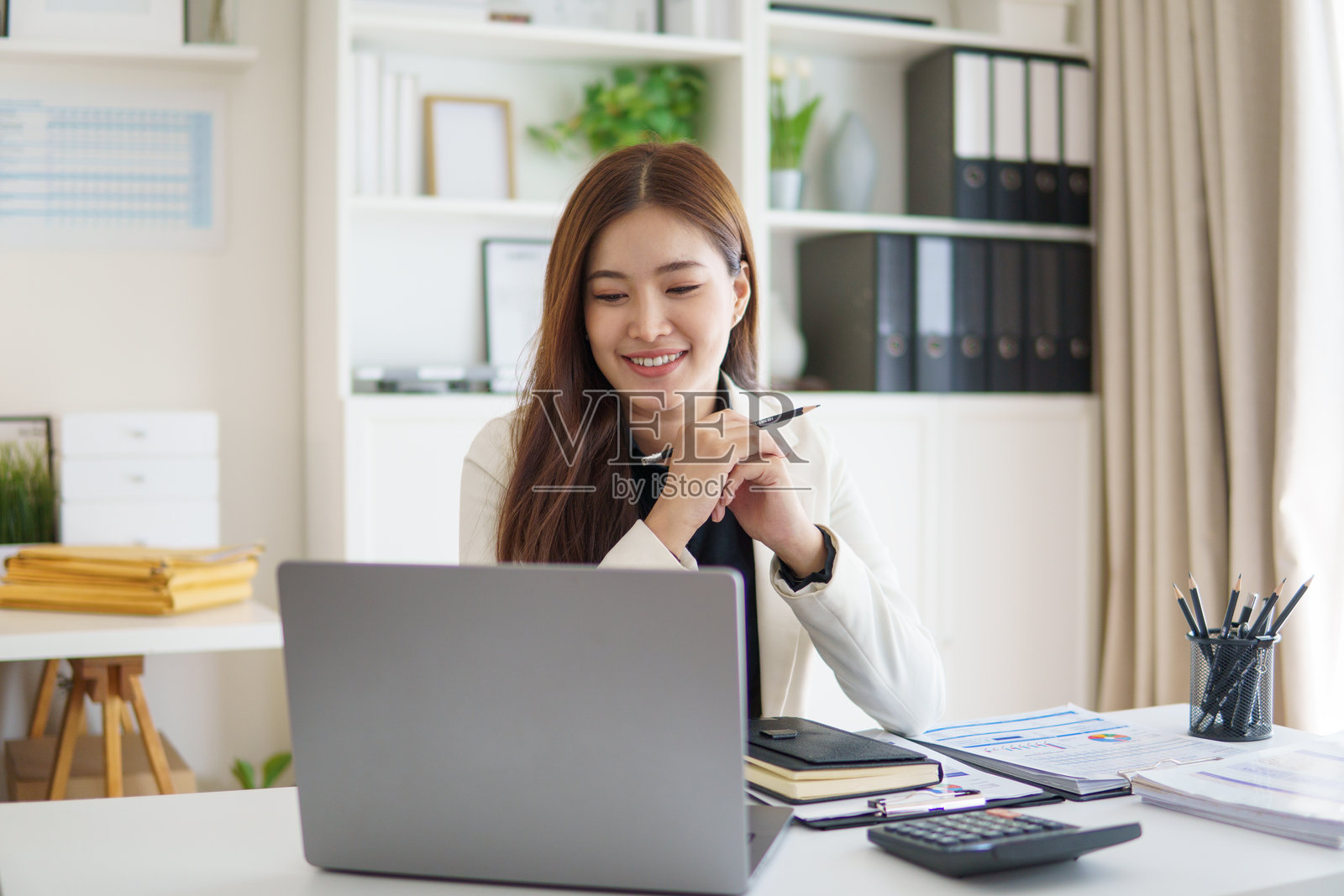 一位微笑着、正在现代办公室里通过笔记本电脑参加在线会议的商业女性。照片摄影图片