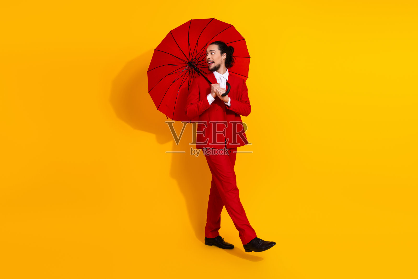 身着亮眼红色西装的男人，手持雨伞，在明亮的黄色工作室中，打造出大胆的时尚造型，彰显现代魅力与假日风格的冒险气息。照片摄影图片