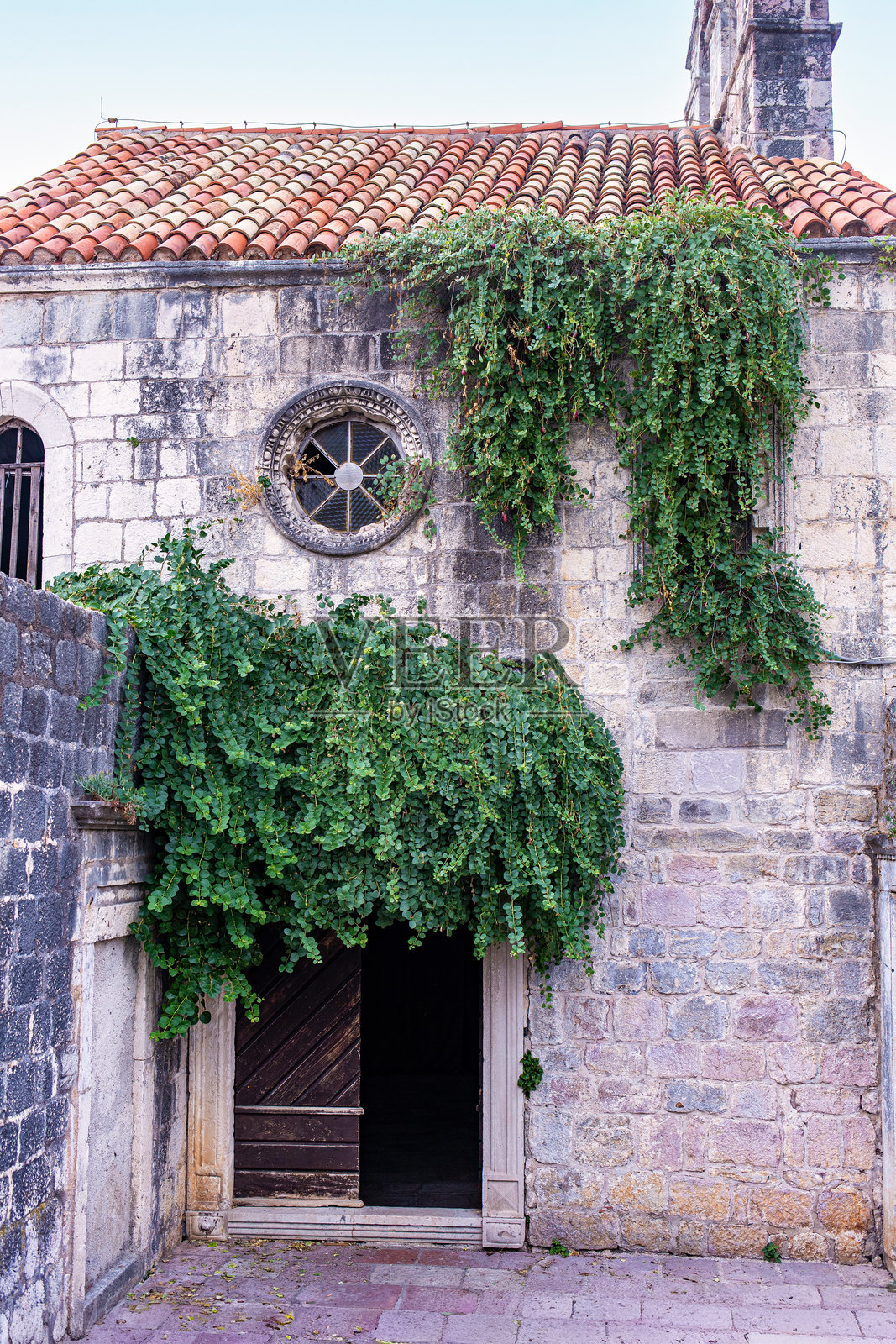 布德瓦老城，带有拱形木门和茂盛绿藤的老石建筑立面照片摄影图片