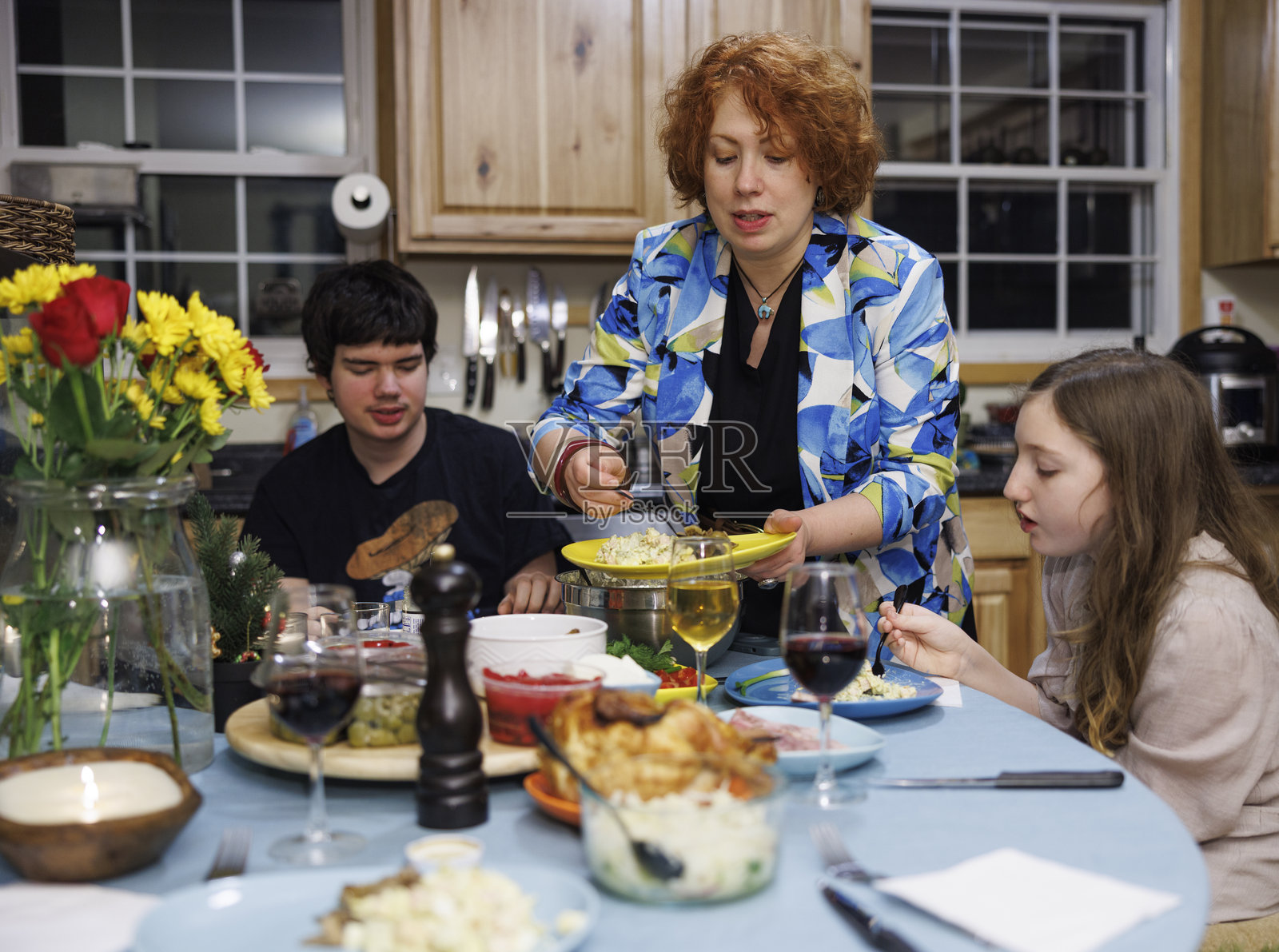 家庭聚餐，包括一位自闭症青少年和一位年幼的女儿。中年红发妈妈在晚餐聚会时，在家里的厨房里分发食物。照片摄影图片