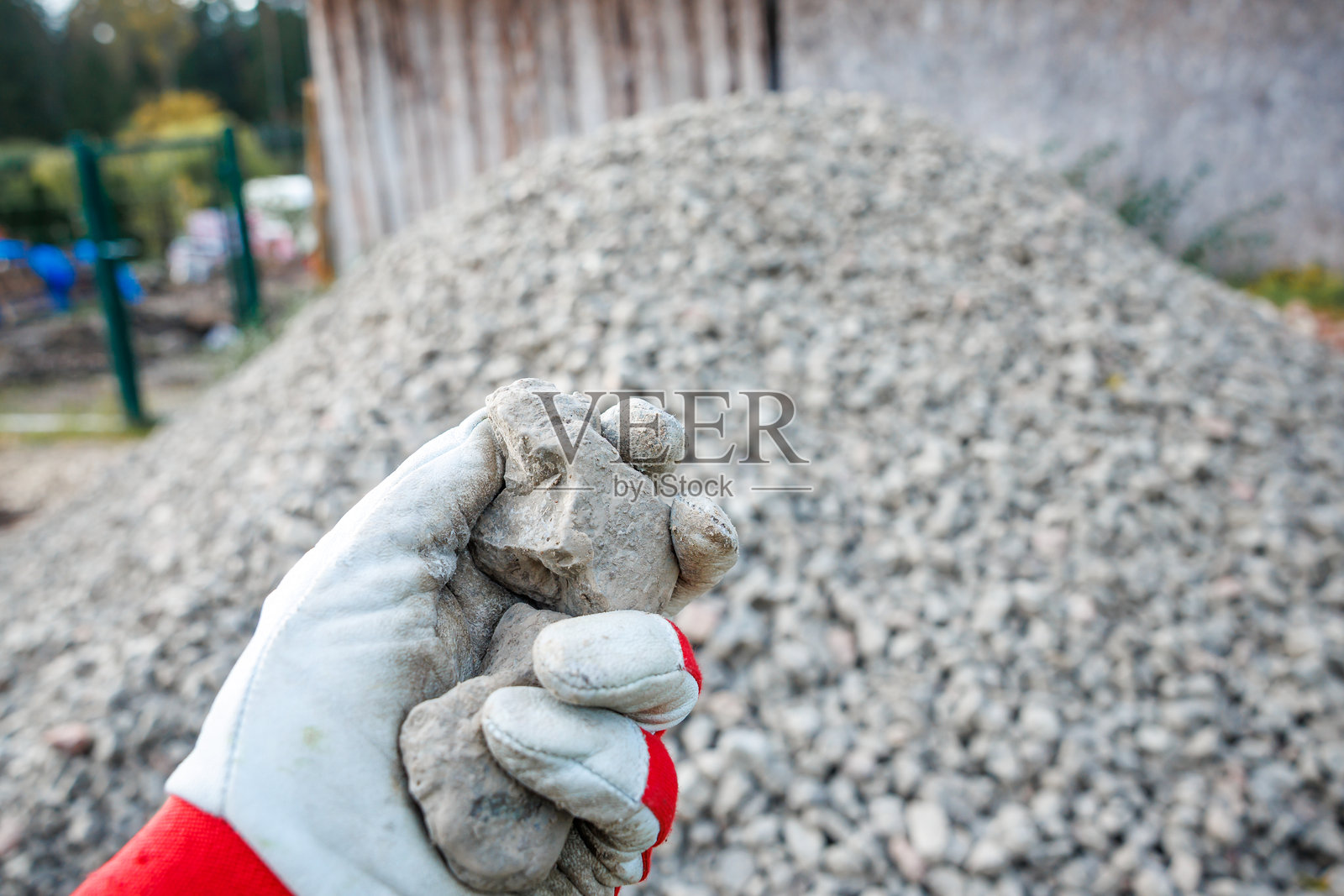 戴手套的手握着碎石，附近有木质结构和栅栏。照片摄影图片