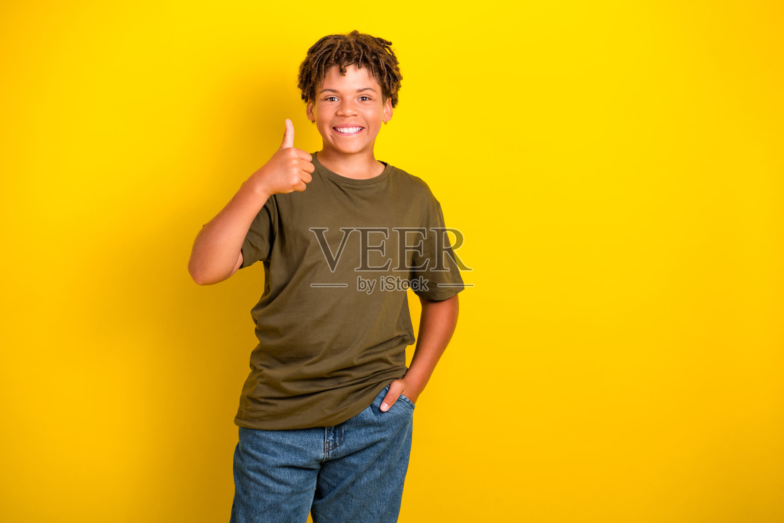 一个穿着休闲卡其色T恤和牛仔裤的快乐小男孩，竖起大拇指，背景是明亮的黄色，非常适合促销、生活方式和广告宣传。照片摄影图片
