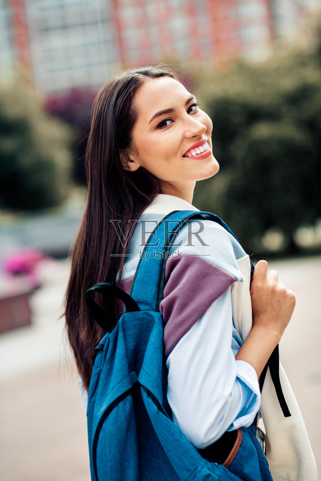 一位背着背包的可爱女士，在阳光明媚的日子里，于休闲的城市环境中自信地微笑照片摄影图片