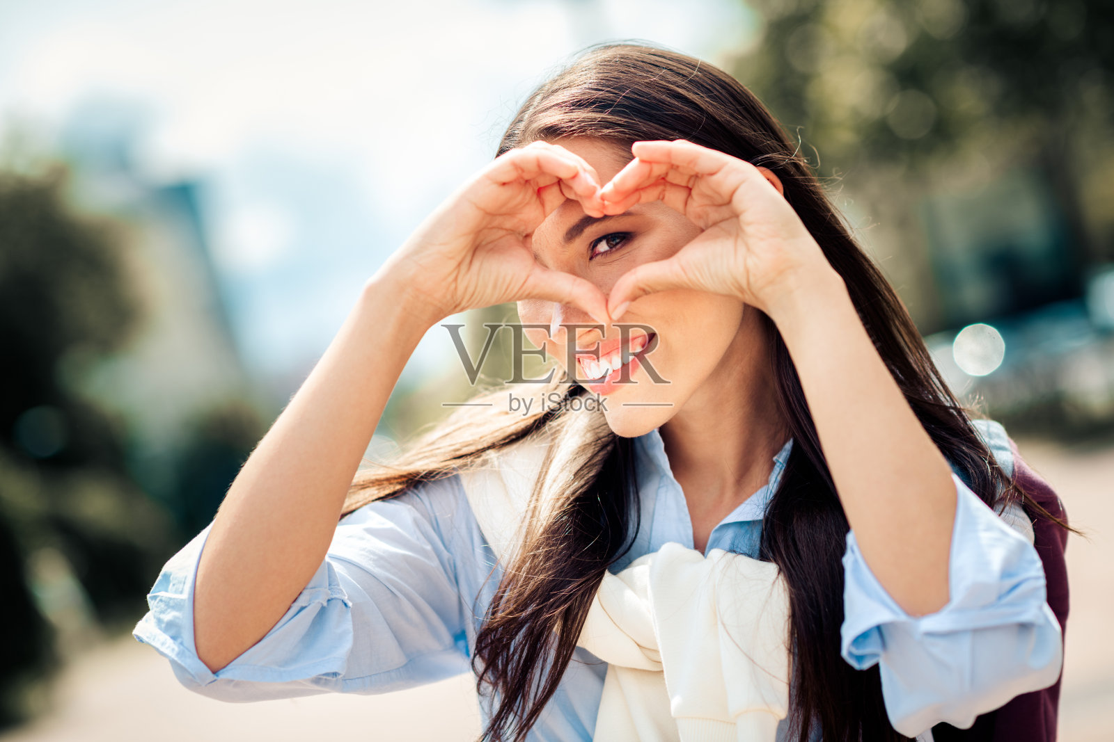 一位迷人的女子在春日休闲的城市户外，双手比心，笑容灿烂照片摄影图片