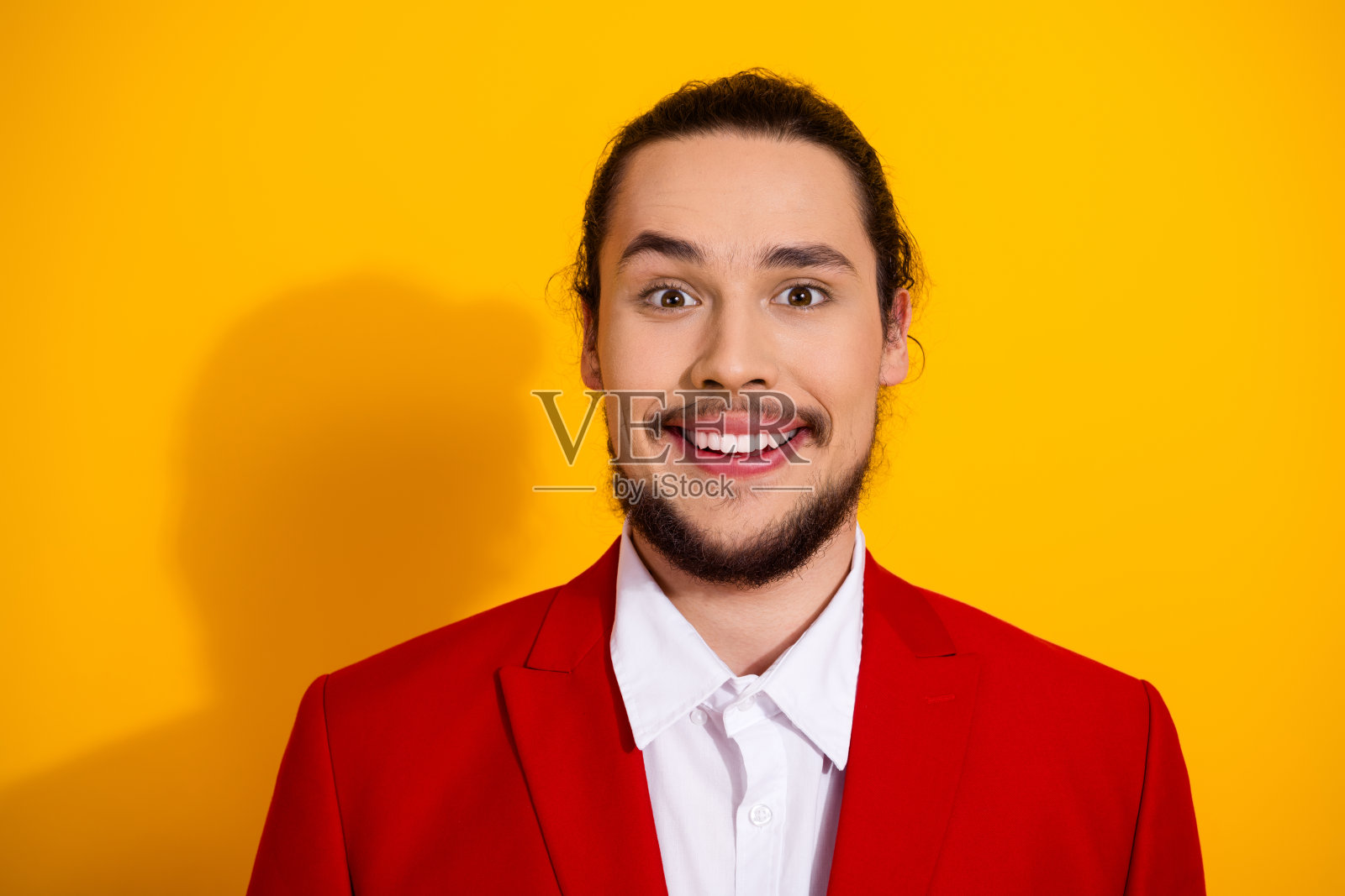 穿着时尚红色套装的有趣男士在明亮的黄色背景影棚中微笑，用于时尚广告和节日宣传照片摄影图片
