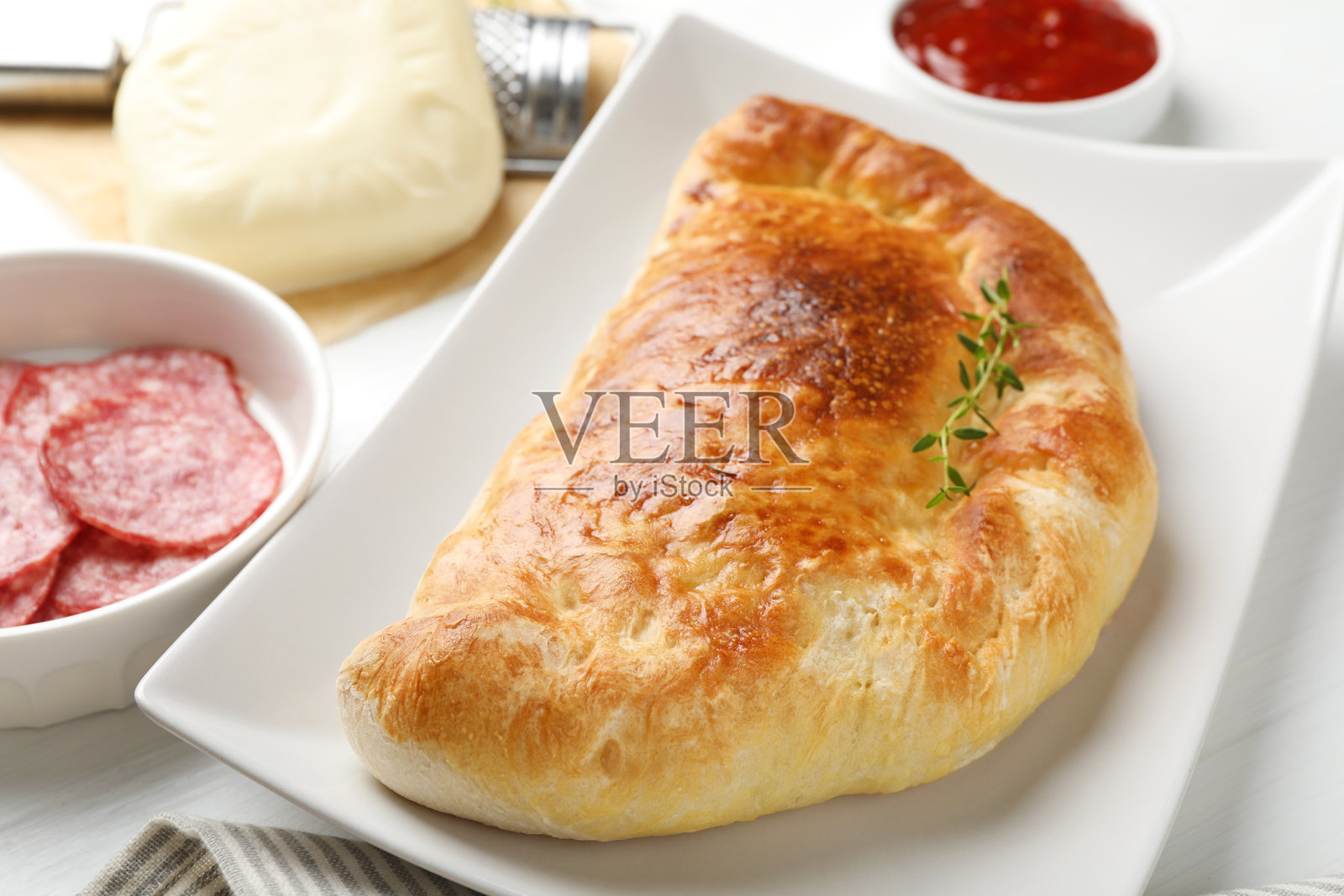 白色桌面上美味新鲜的卡尔佐内披萨和食材，特写照片摄影图片