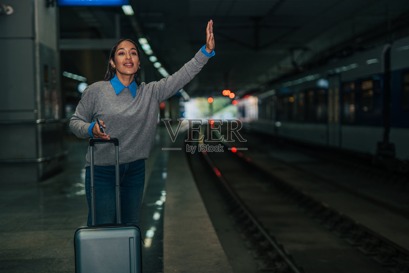 女士在站台上招手示意火车停下，准备出行。照片摄影图片