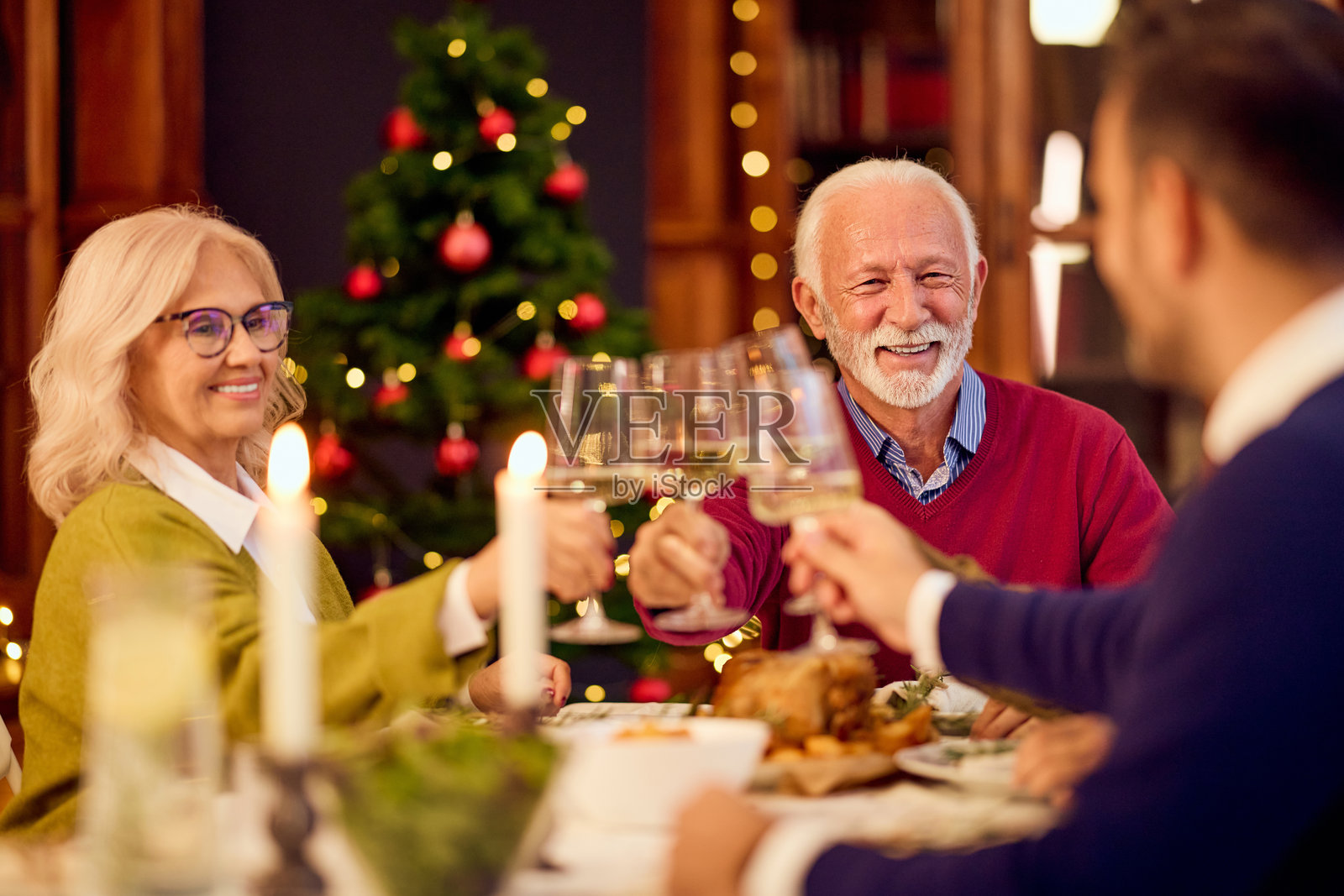 一家人在圣诞晚餐上举起酒杯庆祝，背景是圣诞树照片摄影图片