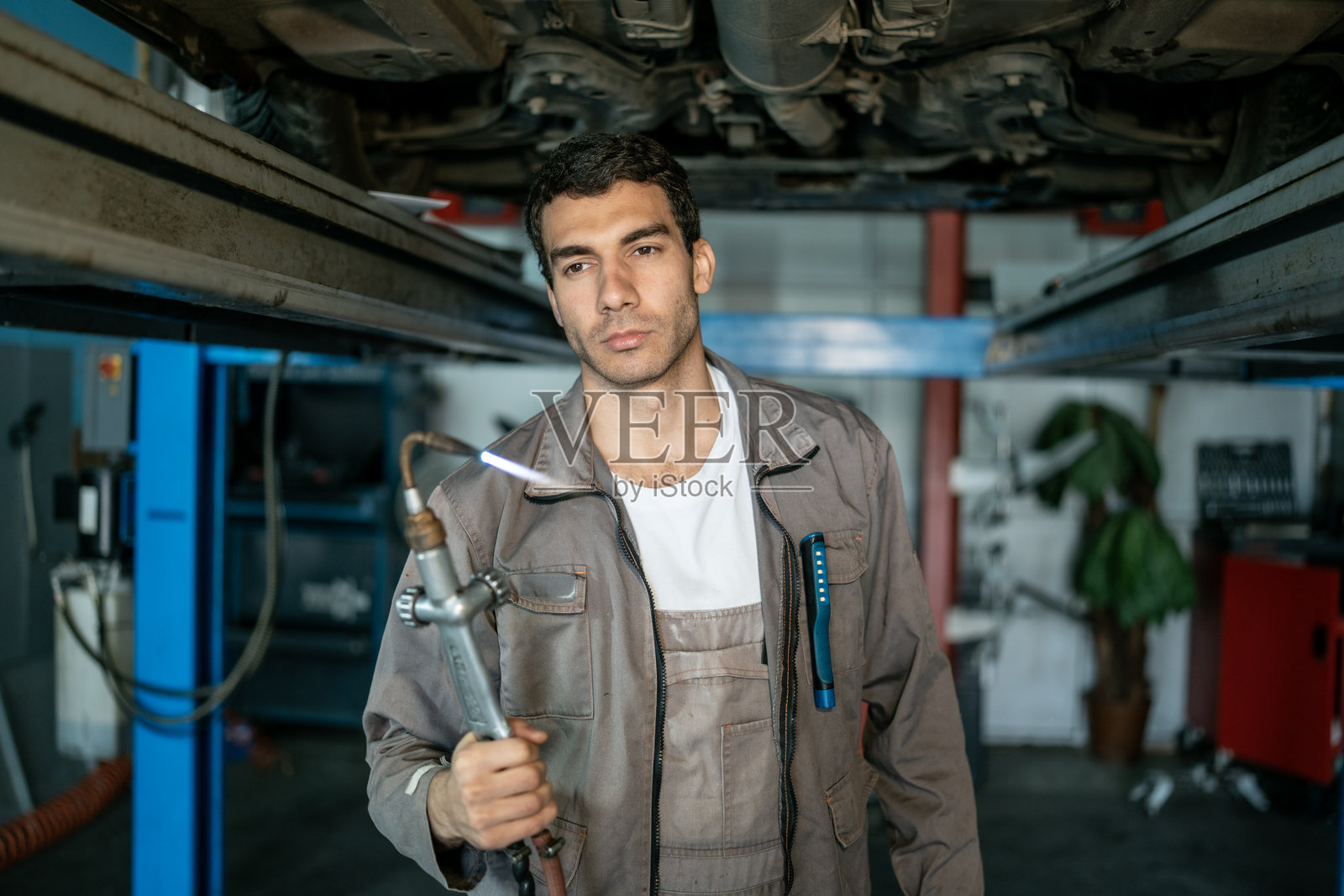 在繁忙的汽车修理车间，专业汽车修理工在汽车举升机下使用焊接炬照片摄影图片