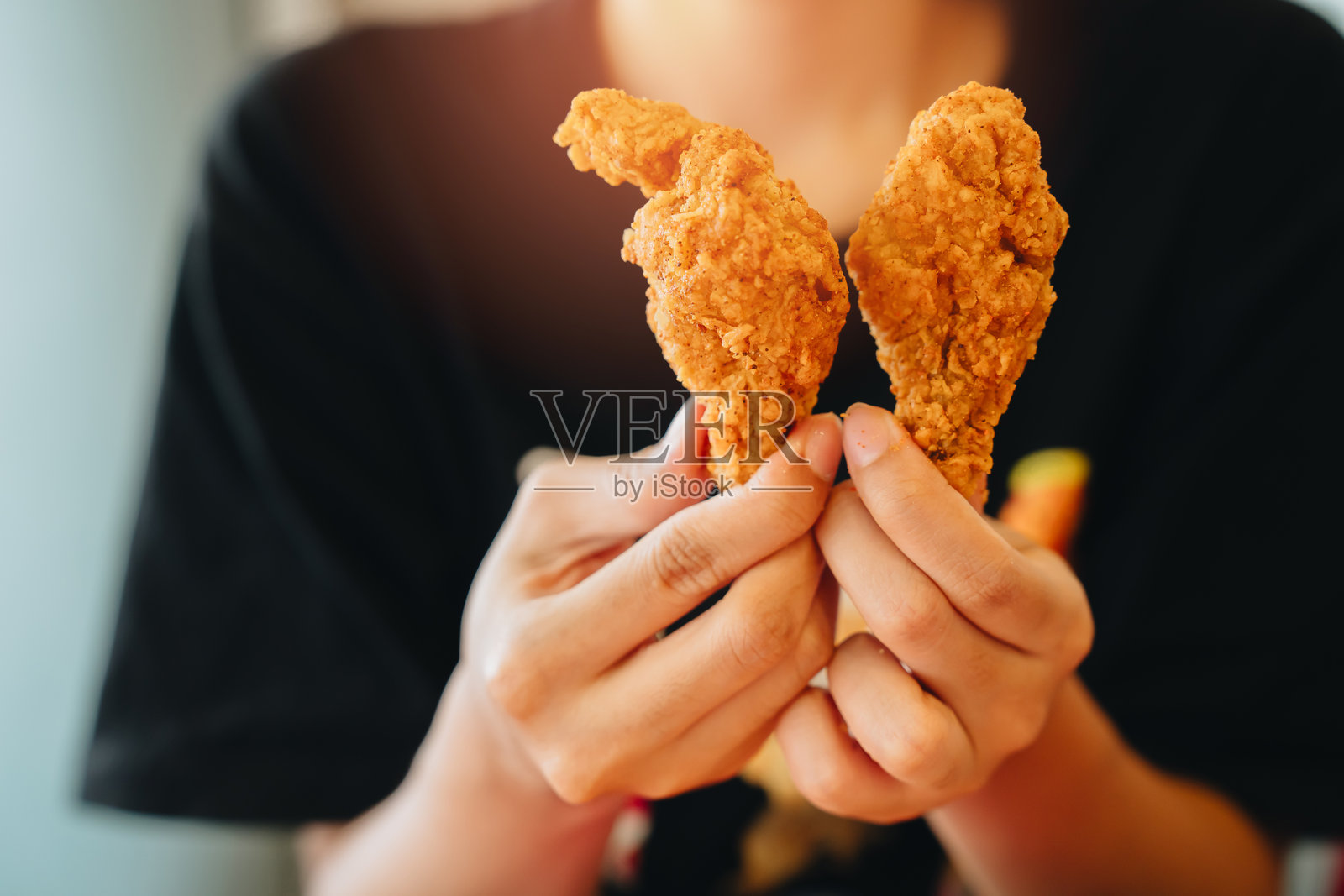 炸鸡概念。休闲黑衬衫人士手持香脆炸鸡翅，特写镜头突出美味诱人的美食照片摄影图片