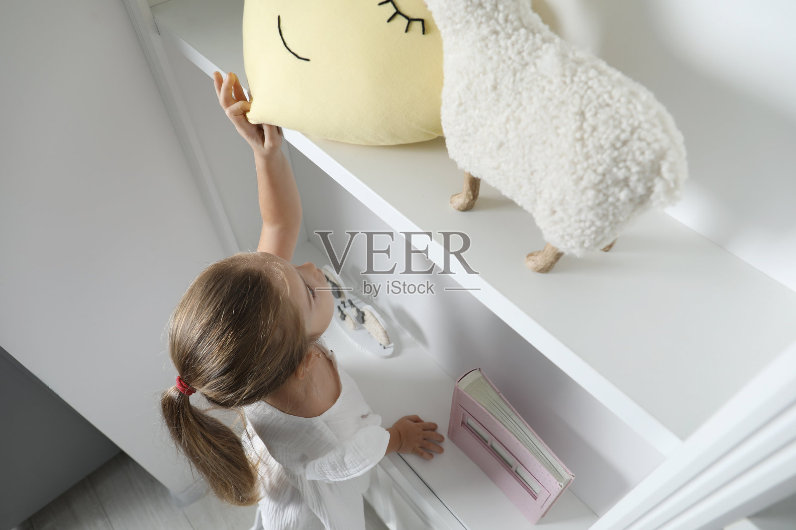 俯视视角，小女孩在室内伸手去拿架子上的玩具照片摄影图片