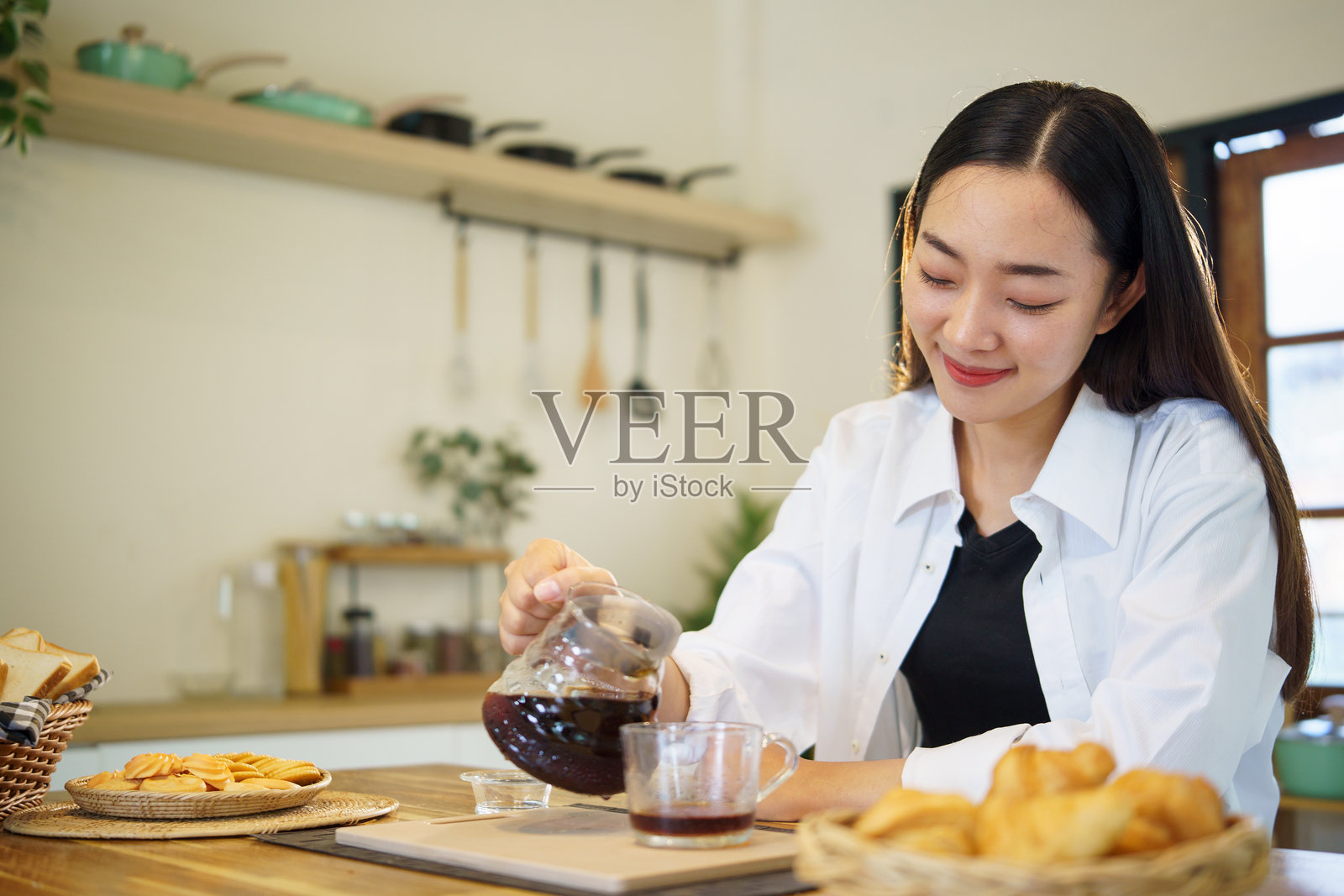 一位女士在厨房里，惬意地享用早晨时光，同时将咖啡倒入玻璃杯中。照片摄影图片