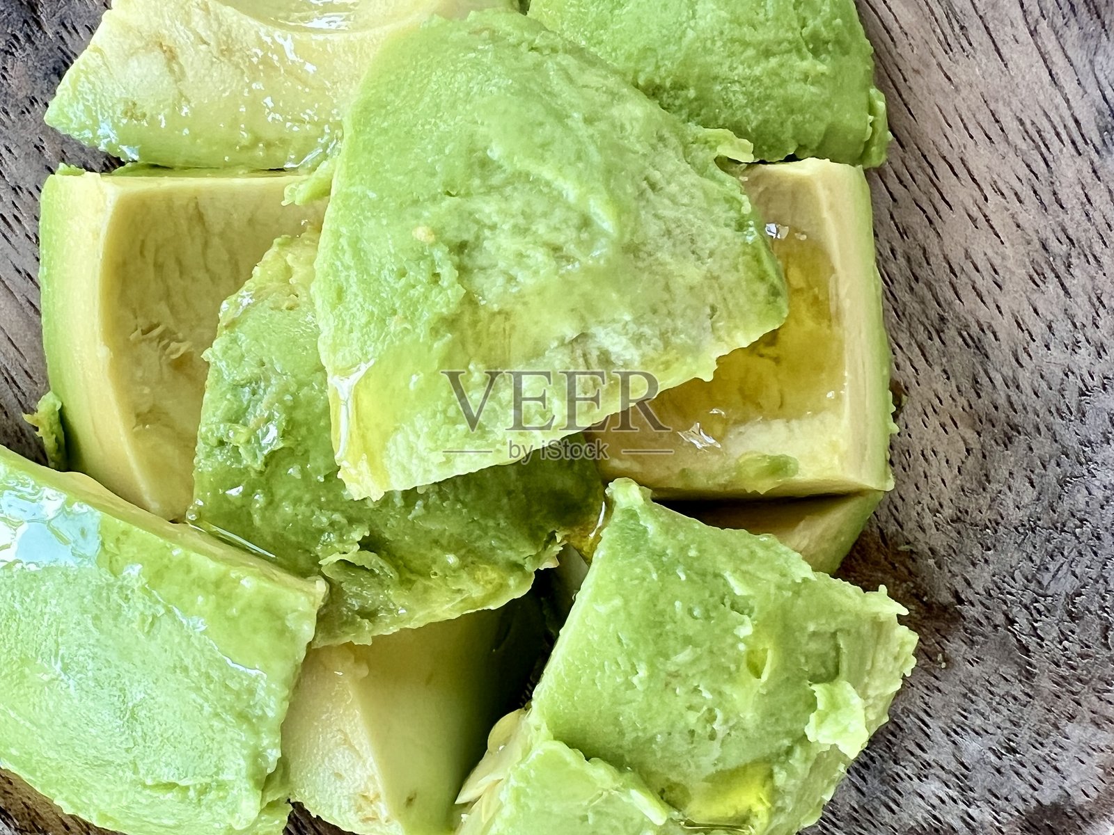 一个旧木盘上放着切好的牛油果，淋上橄榄油。照片摄影图片