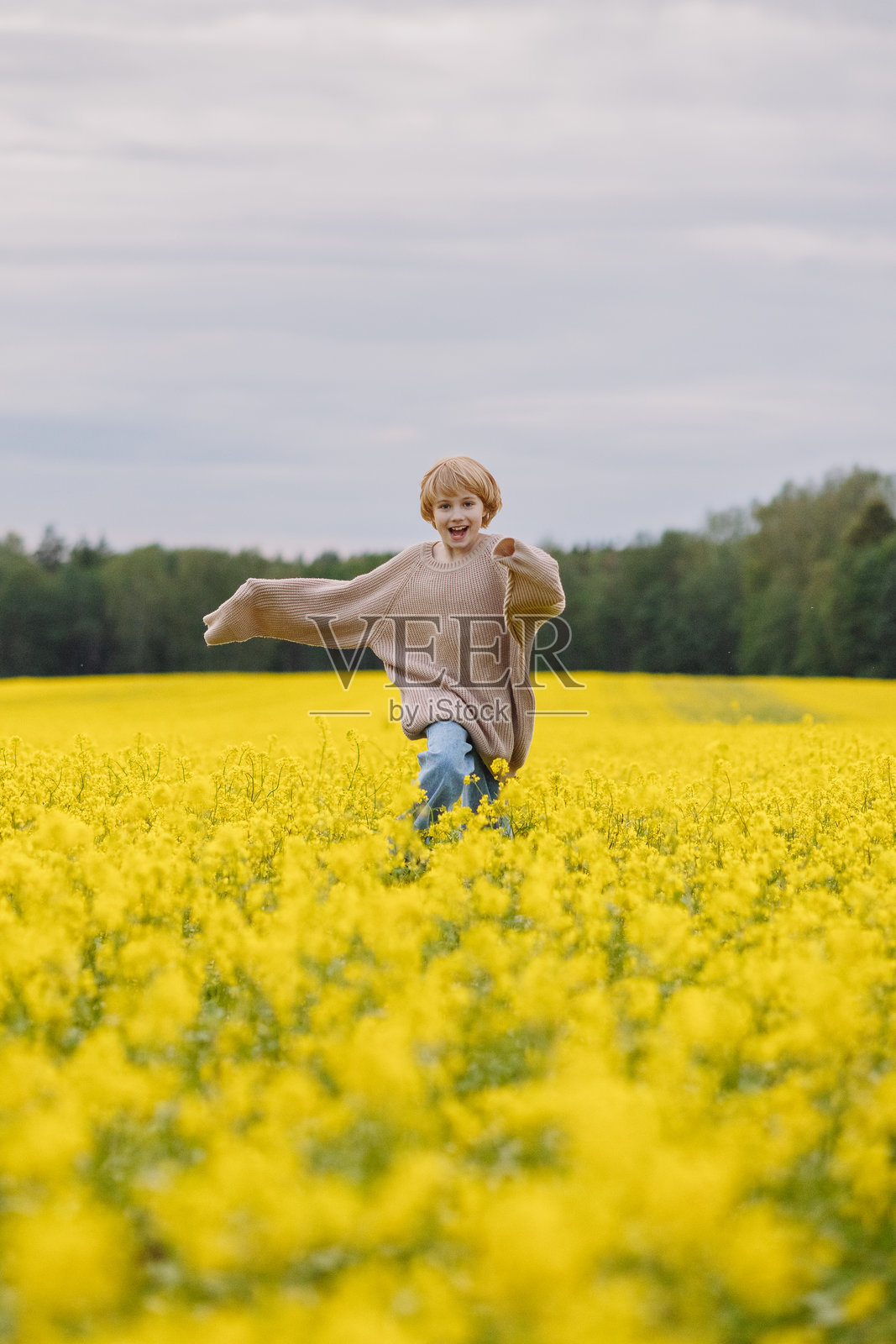 穿着宽大毛衣的9岁女孩在黄色油菜花田里奔跑，脸上带着笑容照片摄影图片