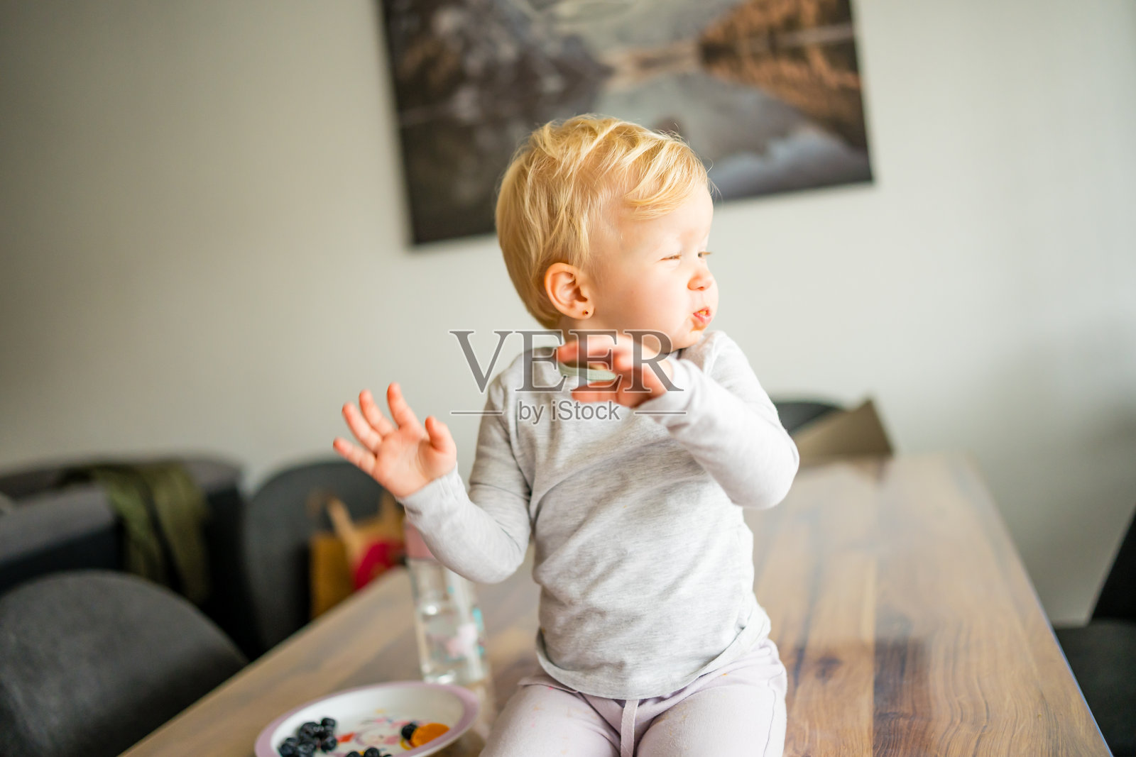 室内，一个幼儿一边嚼着水果一边做着手势照片摄影图片