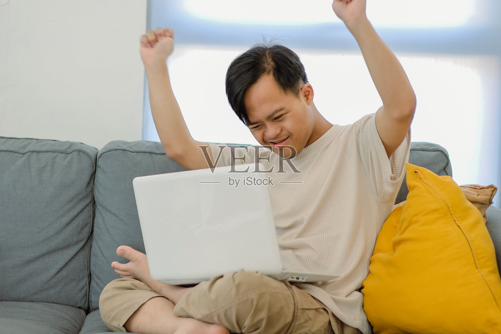 有特殊需求的学生男孩在笔记本电脑上庆祝成功，同时在沙发上放松照片摄影图片