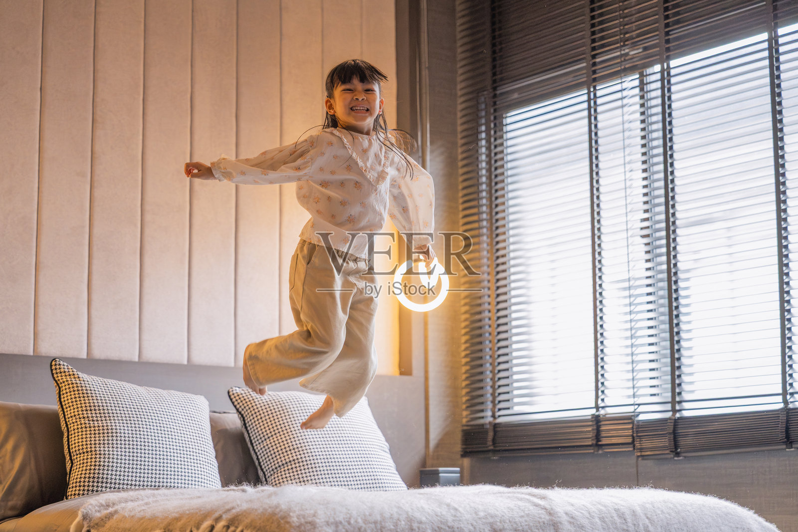 一个俏皮幽默的亚洲小女孩在她卧室的柔软舒适的床上快乐地享受着美好时光，在早晨的白天里带着微笑和笑声拥抱自由休闲的居家生活。照片摄影图片