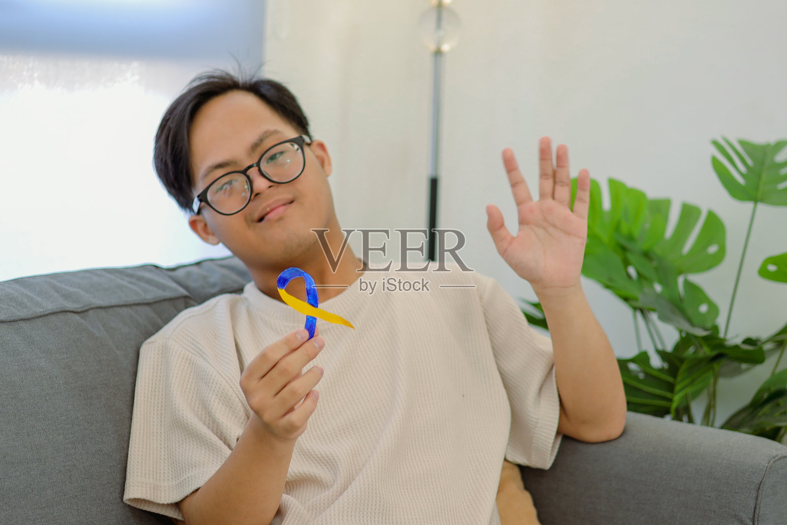 患有唐氏综合征的积极青少年男孩挥手致意，展示着黄蓝丝带以示支持照片摄影图片