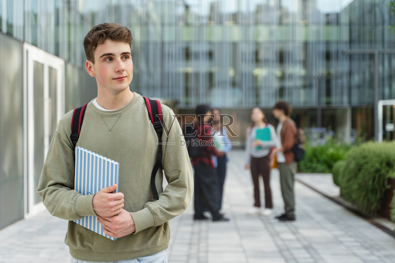 一位思考中的青少年学生站在大学校园里，开心地看向一旁，准备听讲座。照片摄影图片