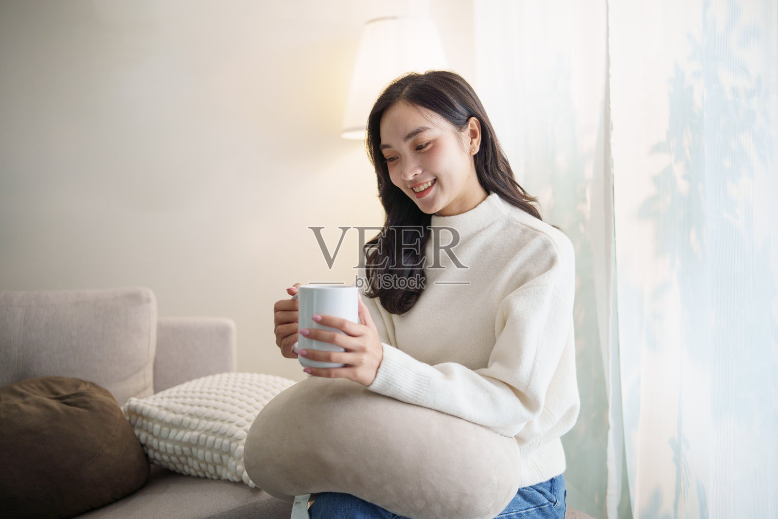 一位女士在窗边，享受着一杯热饮，脸上带着微笑。照片摄影图片