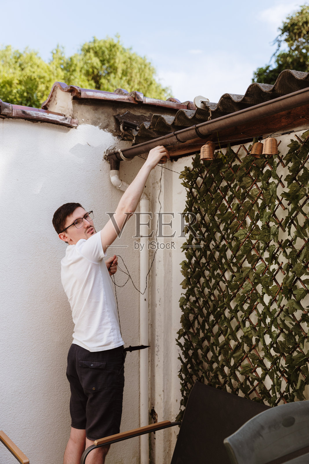 一个年轻男子正在花园小屋上悬挂串灯。照片摄影图片