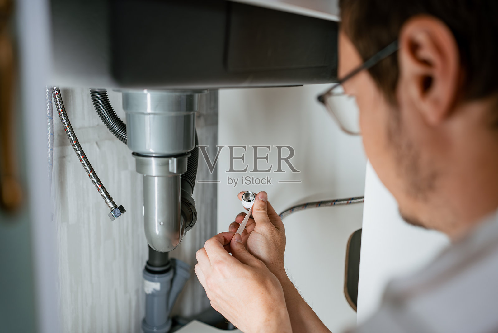 专业水管工在管道螺纹上缠绕特氟龙胶带，为混水阀连接做准备，在住宅厨房环境中确保无泄漏的管道连接照片摄影图片