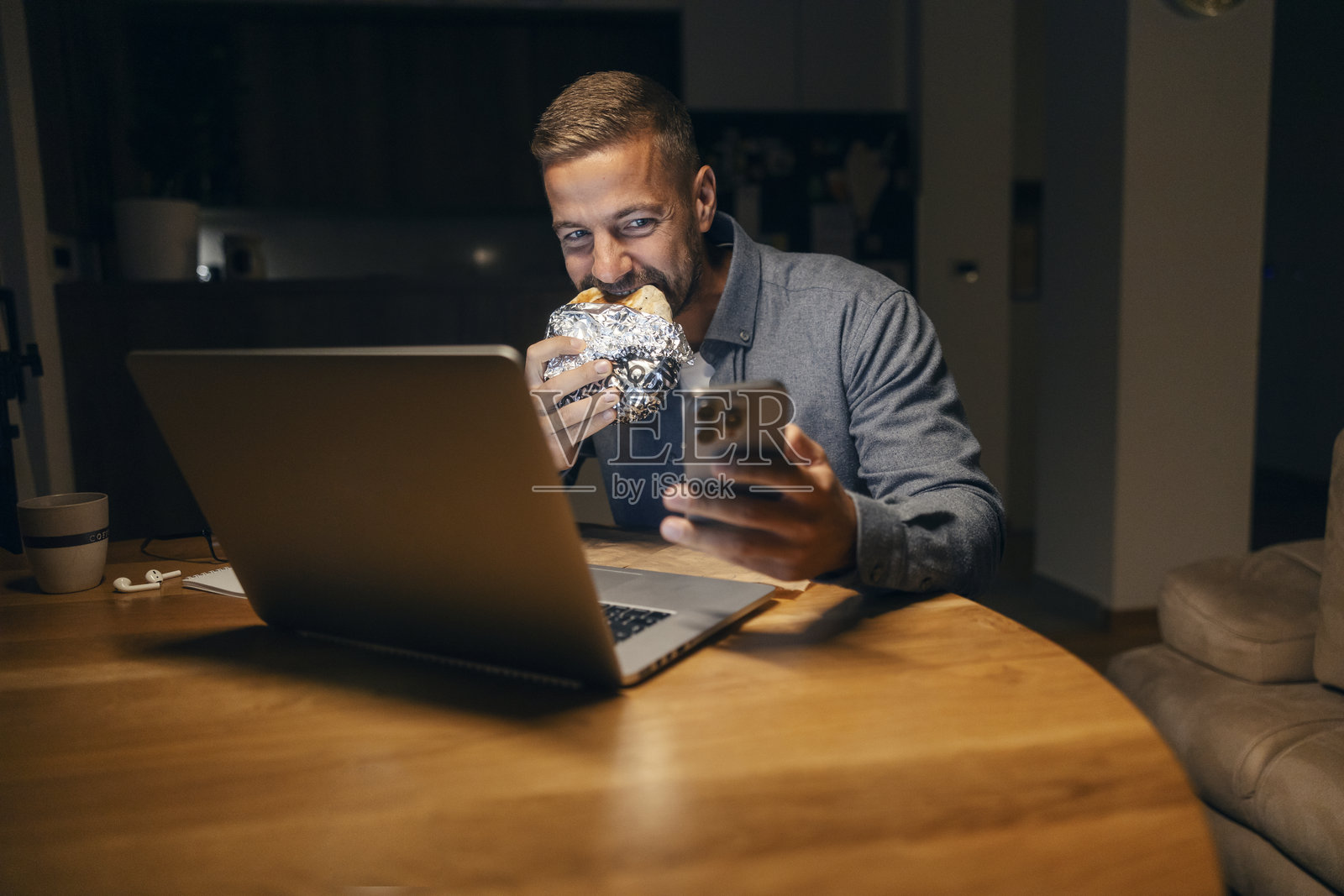 男人一边吃墨西哥卷饼，一边用笔记本电脑和智能手机处理多项任务照片摄影图片