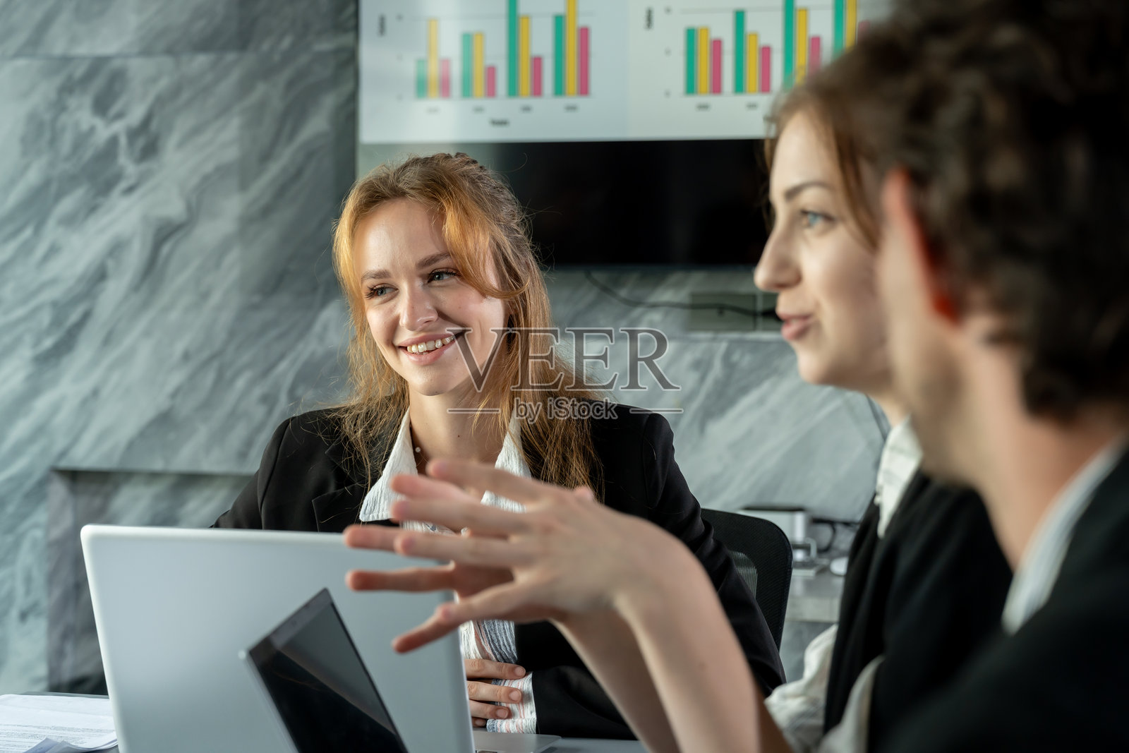 一位白人成年女性高管在现代办公室里，与不同种族背景的同事们一起听取意见，进行商务会议，内容涉及笔记本电脑、团队合作、头脑风暴和办公室工作及商务协作的讨论。照片摄影图片