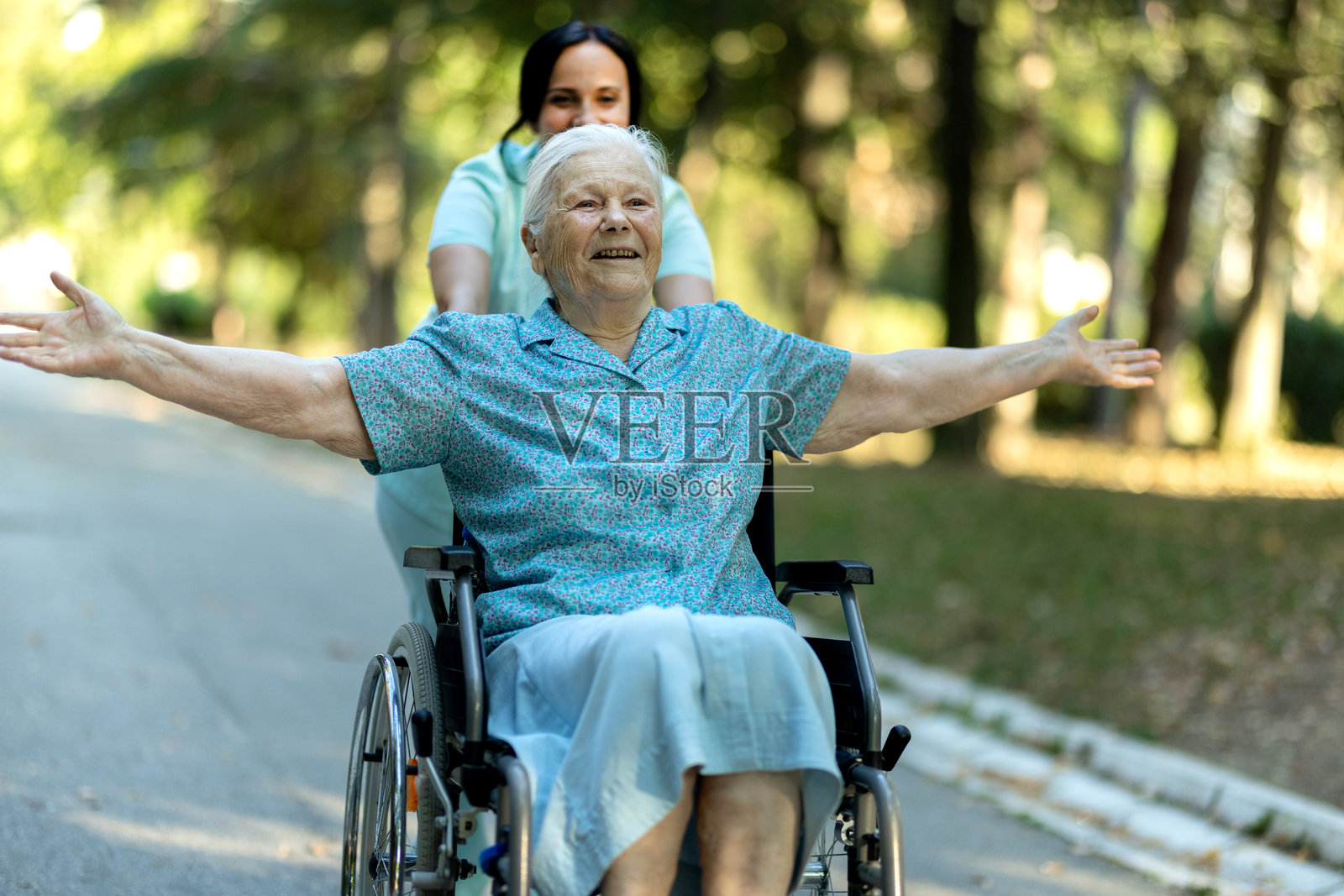 看护者在公园里推着一位坐轮椅的老年妇女照片摄影图片