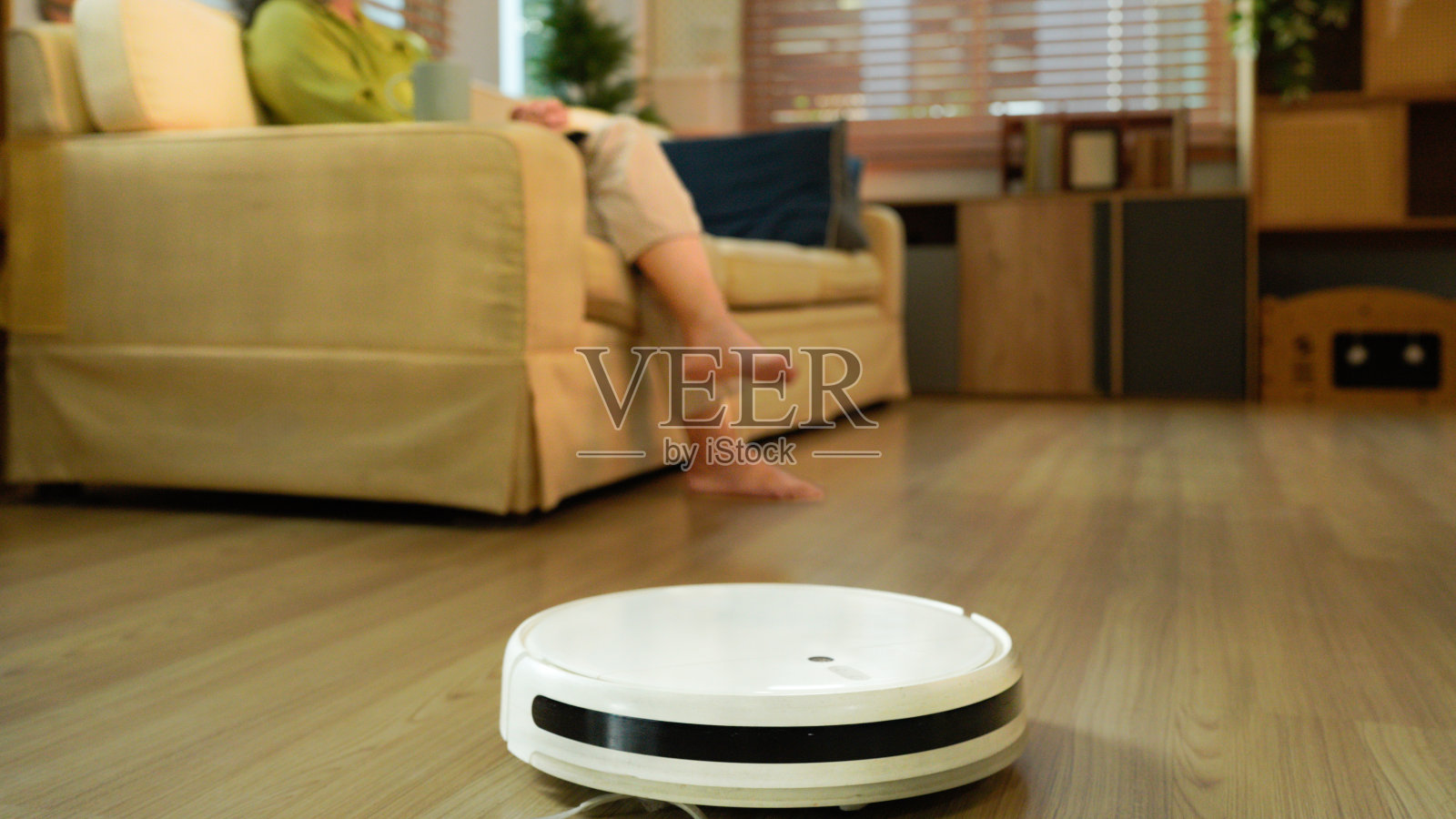 一位年长的女士躺在沙发上，房间里有一个机器人吸尘器照片摄影图片